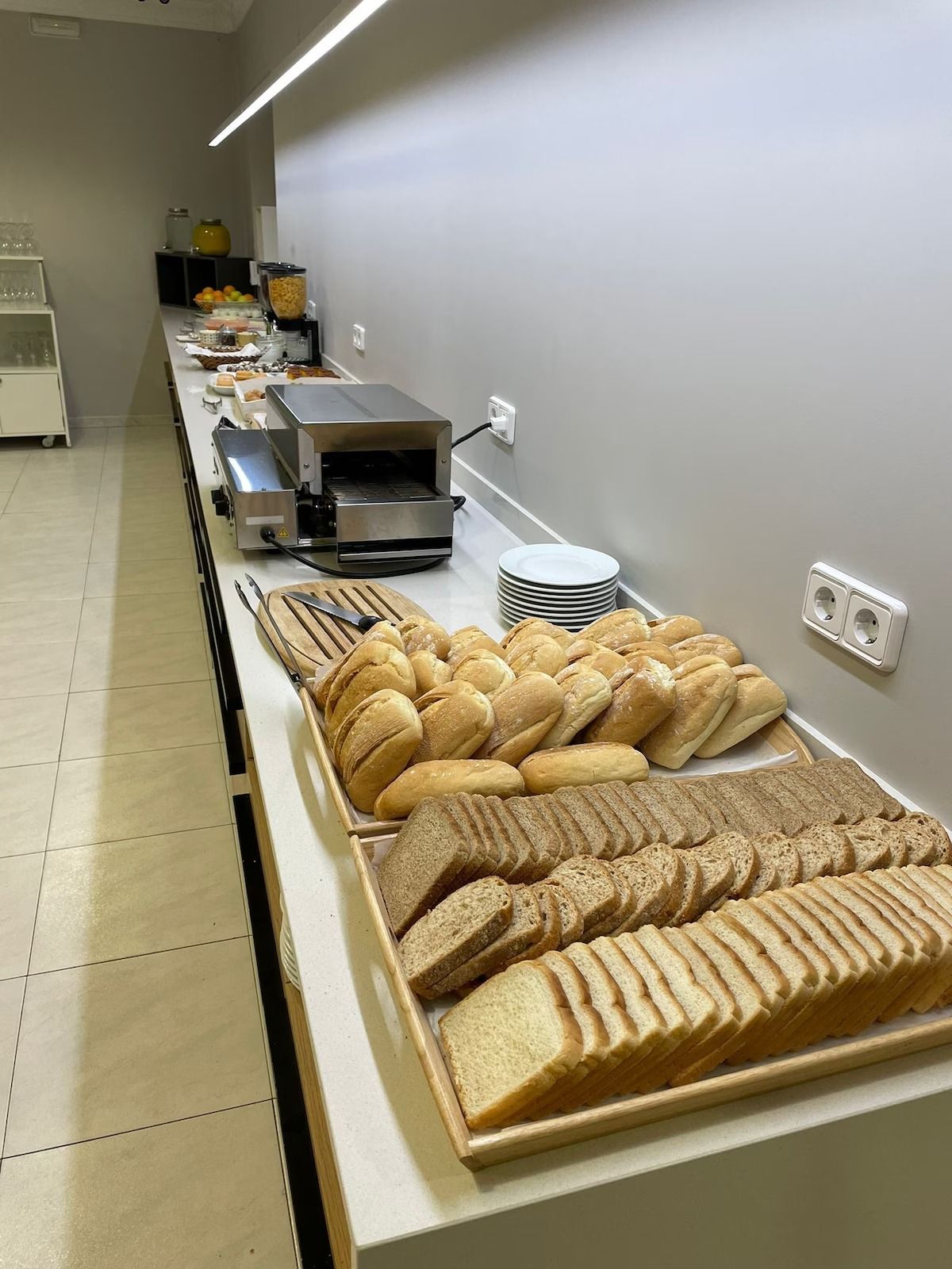 A spacious cafe area featuring multiple round tables, chairs with colorful seats, and a bar with illuminated shelves.