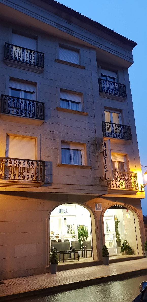 A four-story hotel building with stone walls, balconies, and illuminated ground-floor windows at twilight.