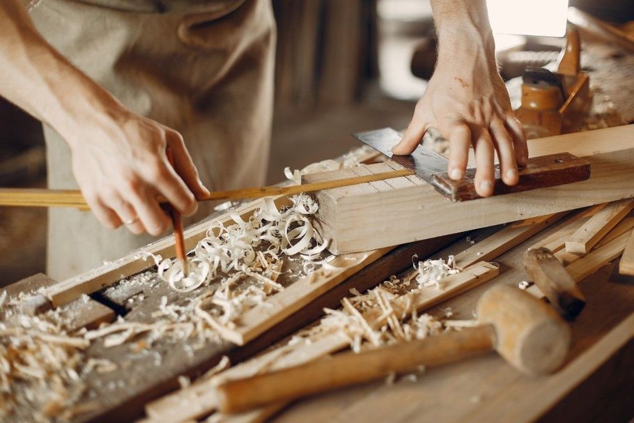 Hands of a person working with wood. Using a pencil, ruler, and plane to shape a wooden plank. Sawdust visible.