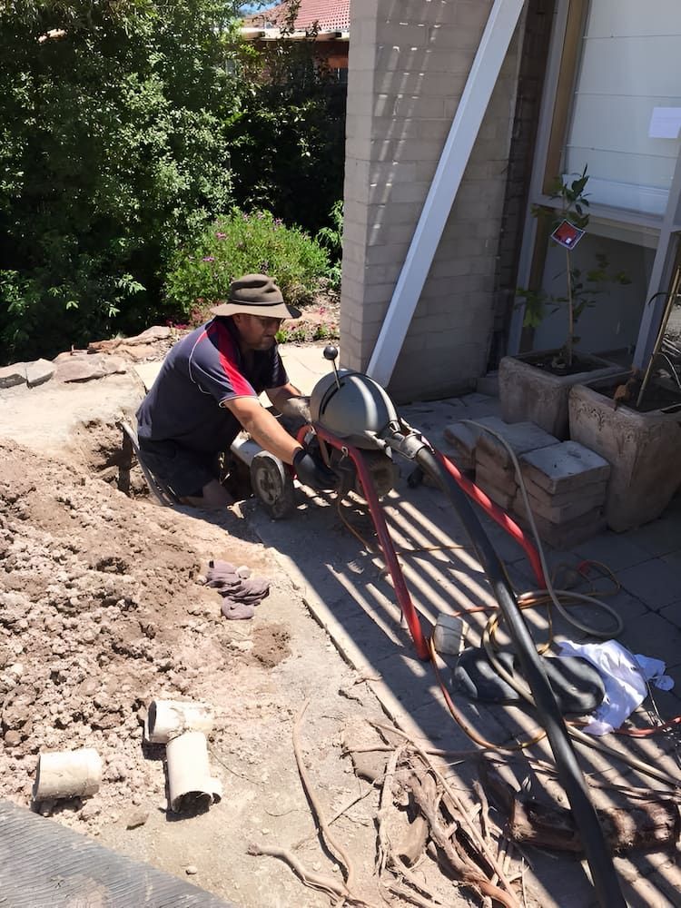 A Man is Kneeling Down in the Dirt Next to a Machine — Around Town Plumbing Services in Canberra, ACT