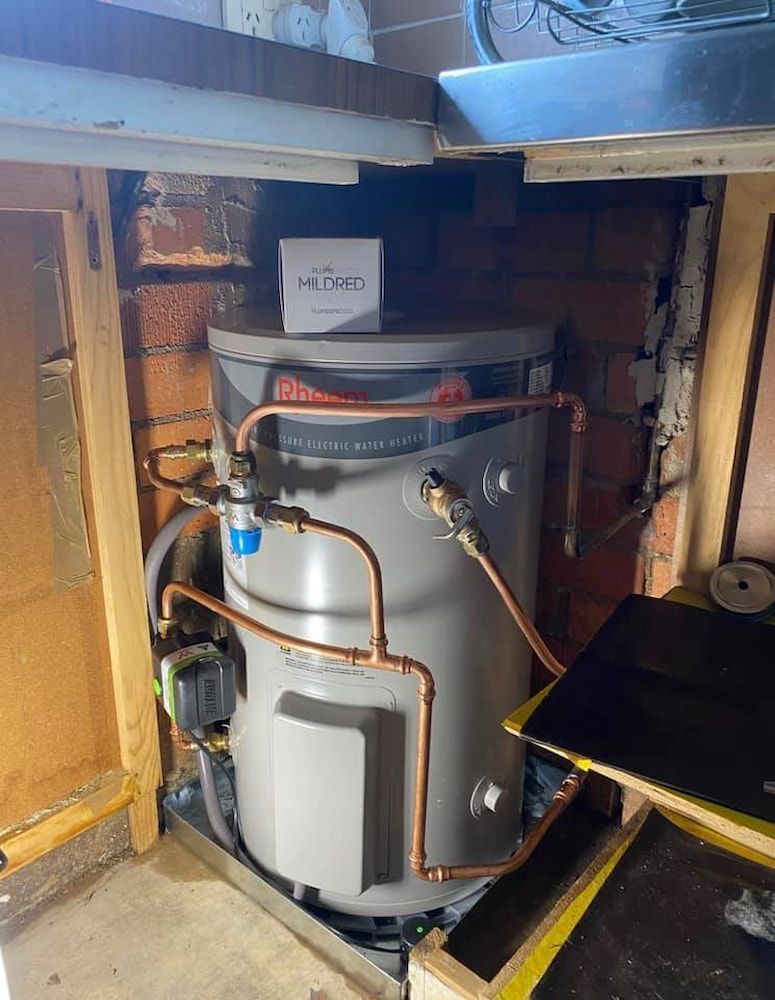 A Water Heater is Sitting Under a Brick Wall in a Room — Around Town Plumbing Services in Canberra, ACT