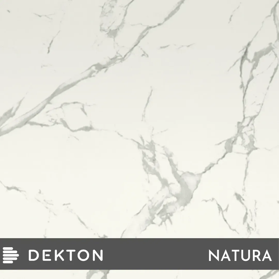 Superficie con aspecto de mármol blanco con vetas grises suaves, etiquetada como Dekton Natura en la parte inferior.