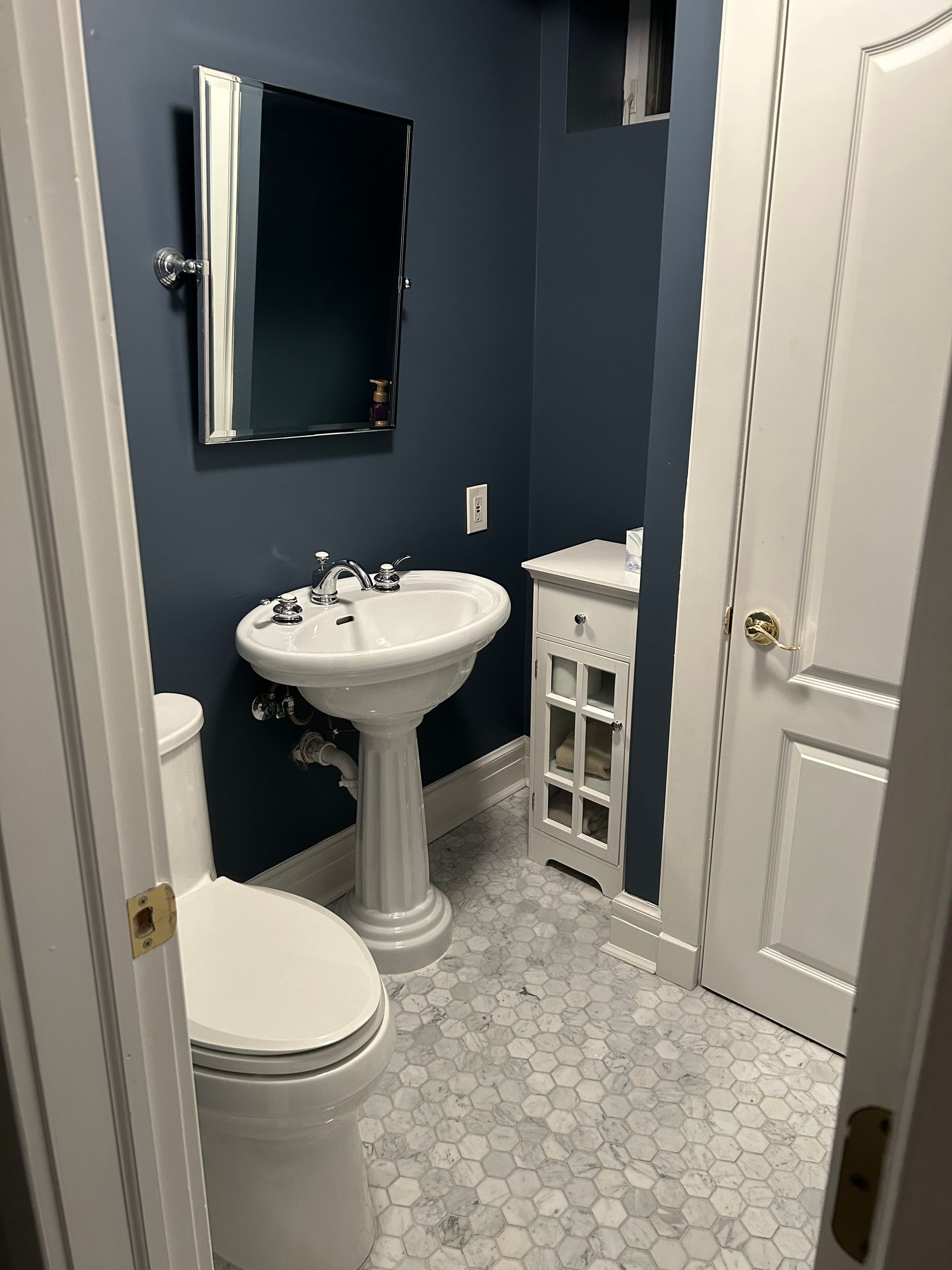 Small bathroom with pedestal sink, toilet, white cabinet, and blue walls.