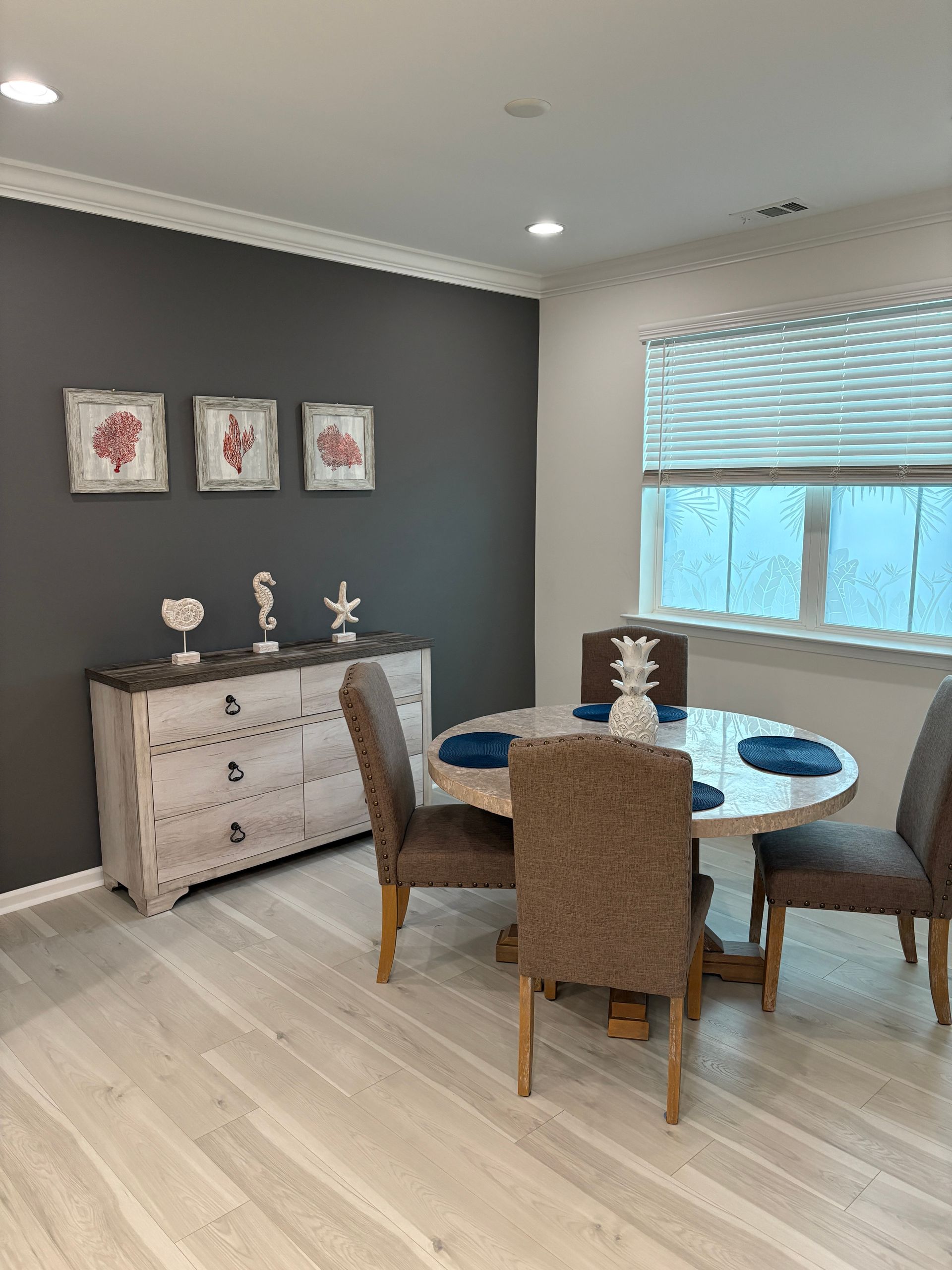 Dining room with round table, four chairs, buffet, and framed artwork on dark gray accent wall.