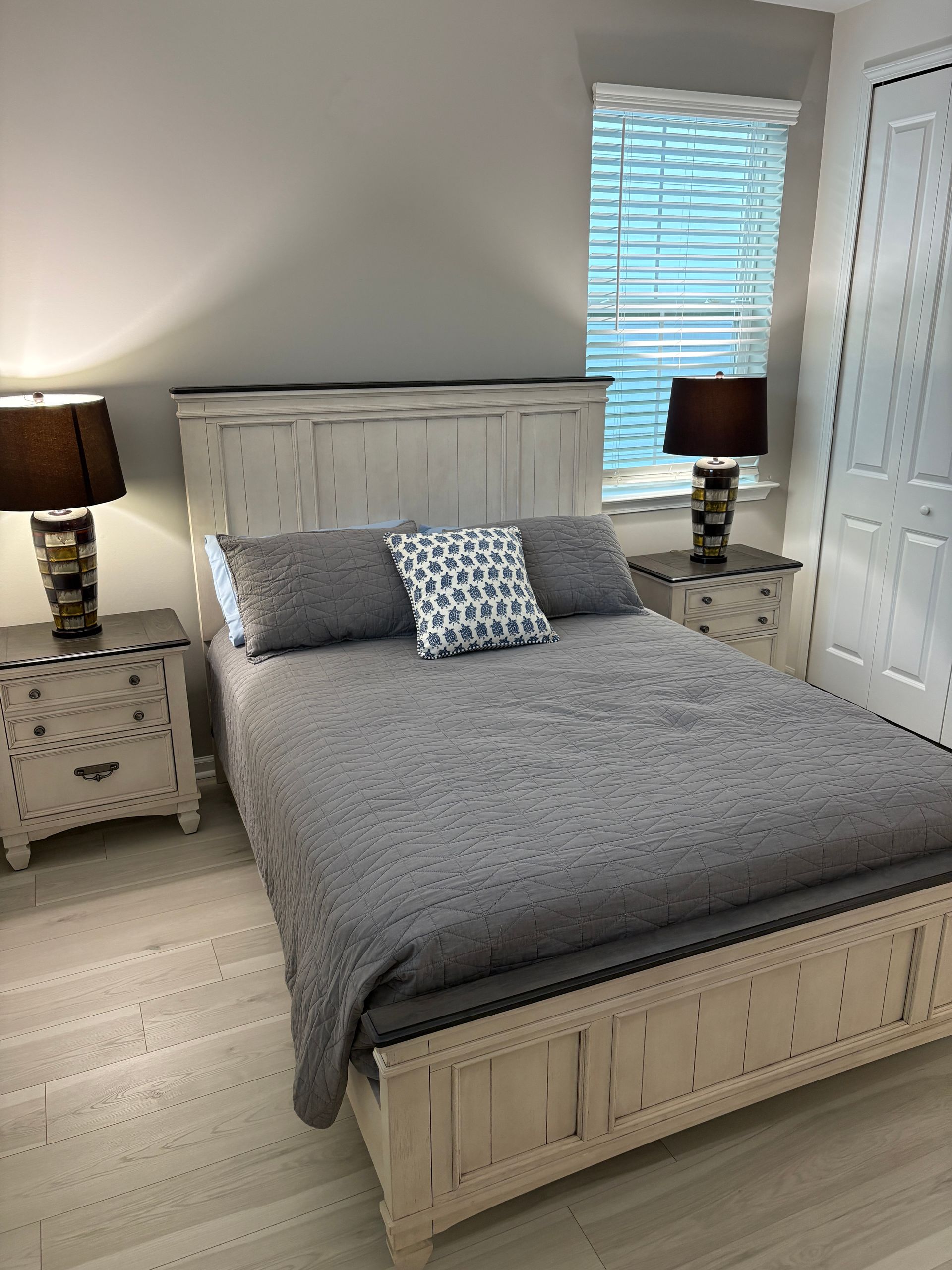 Bedroom with white distressed furniture, grey bedding, and two bedside lamps.