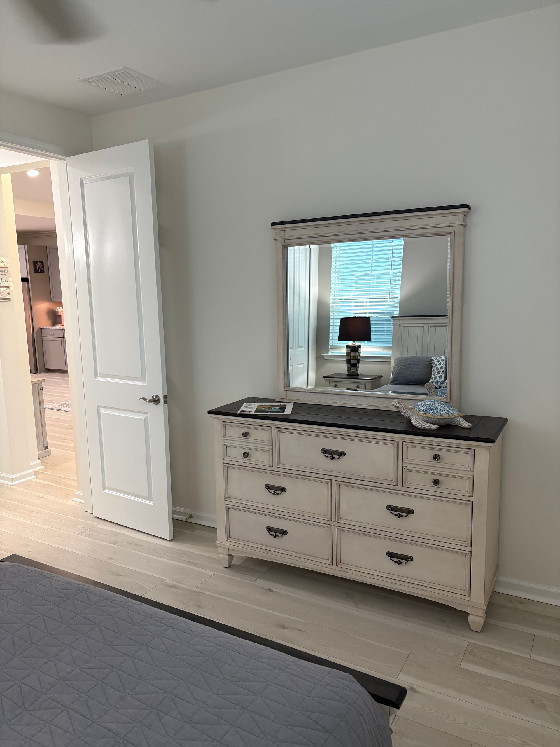 Bedroom with white dresser, mirror, and open door to hallway. Light wood flooring and neutral walls.