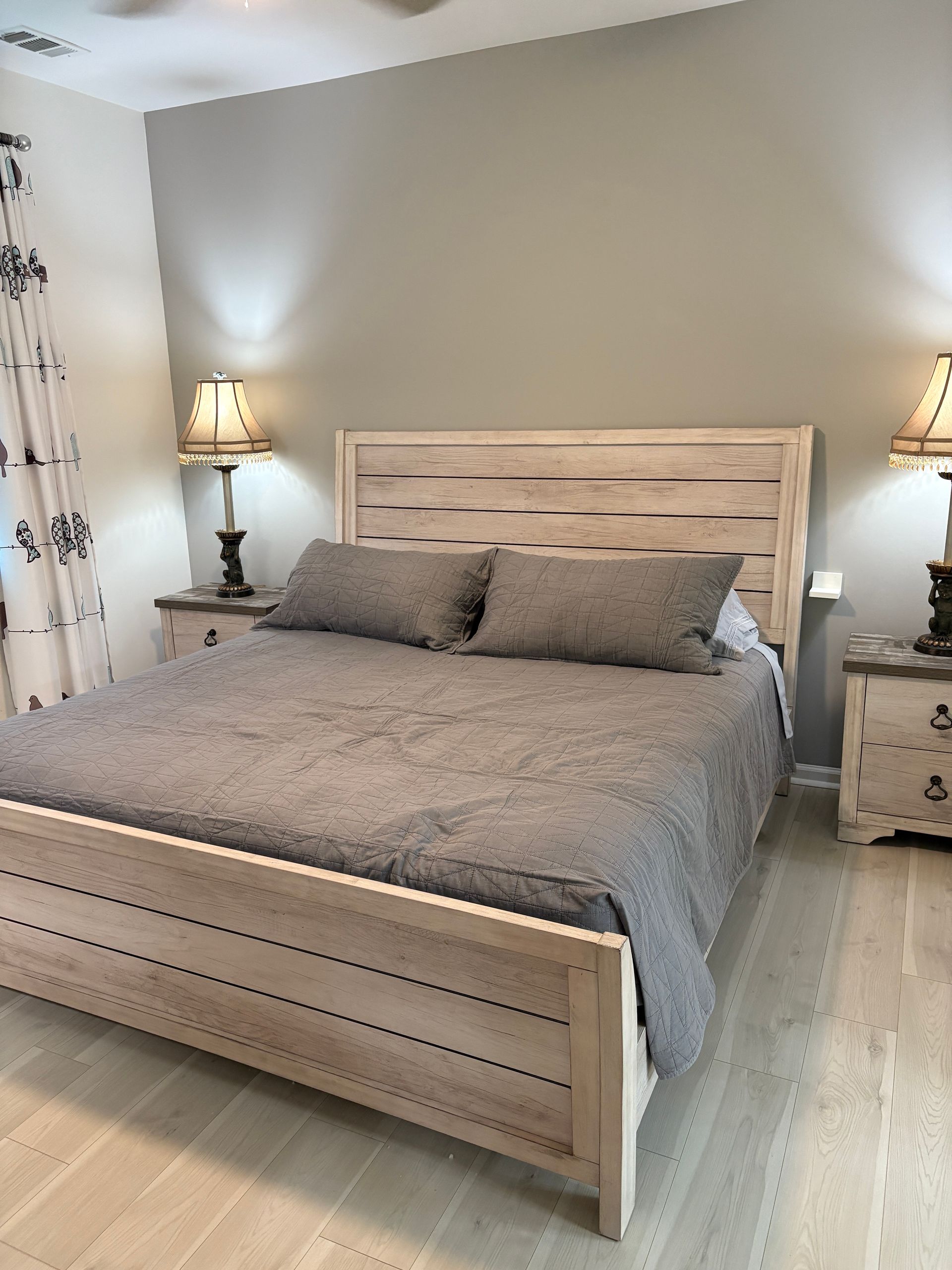Bedroom with king-size bed, gray bedding, two matching nightstands with lamps, and light-colored walls and floor.