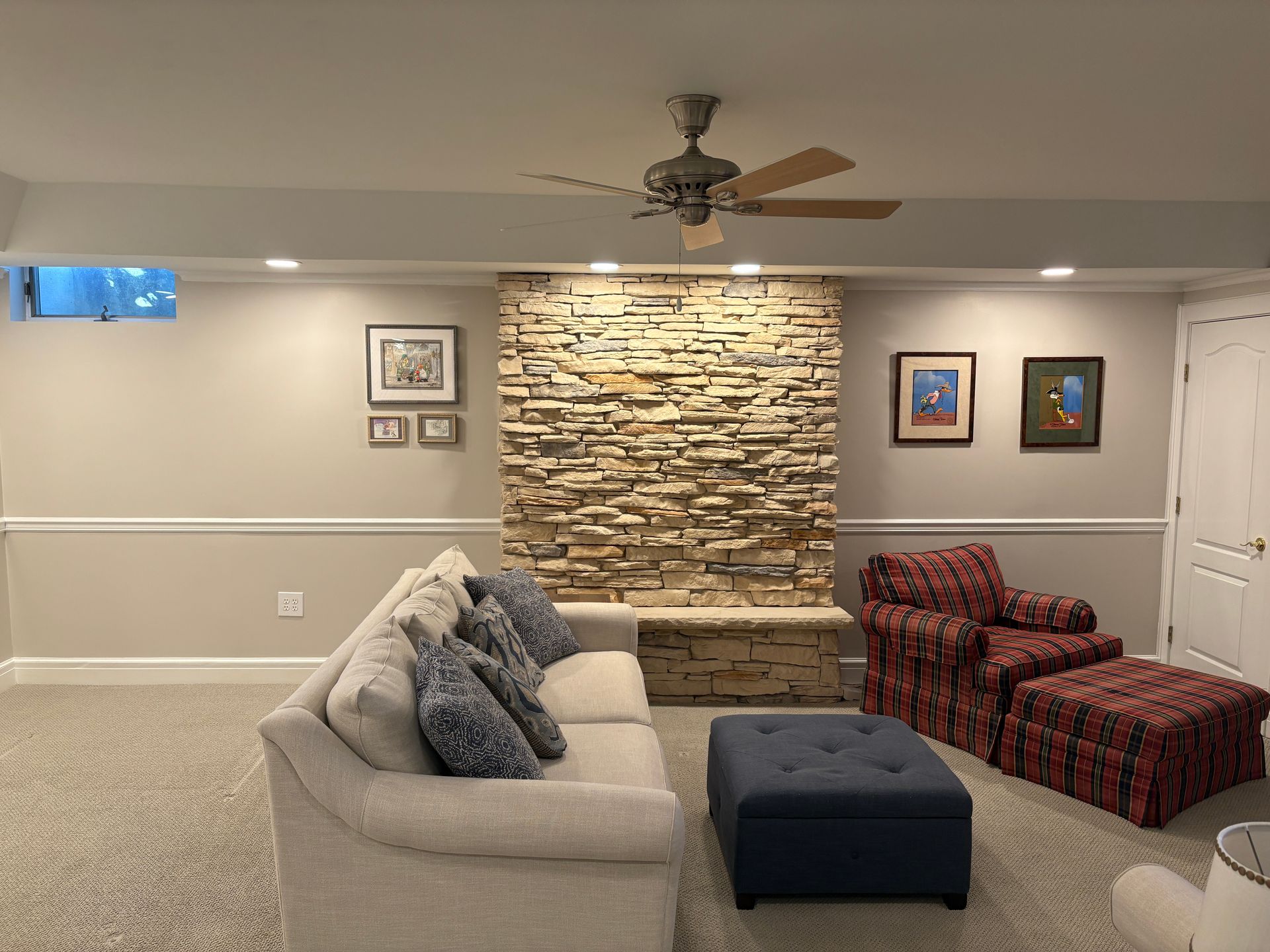 Living room with stone fireplace, beige sofa, red patterned armchair, and blue ottoman.