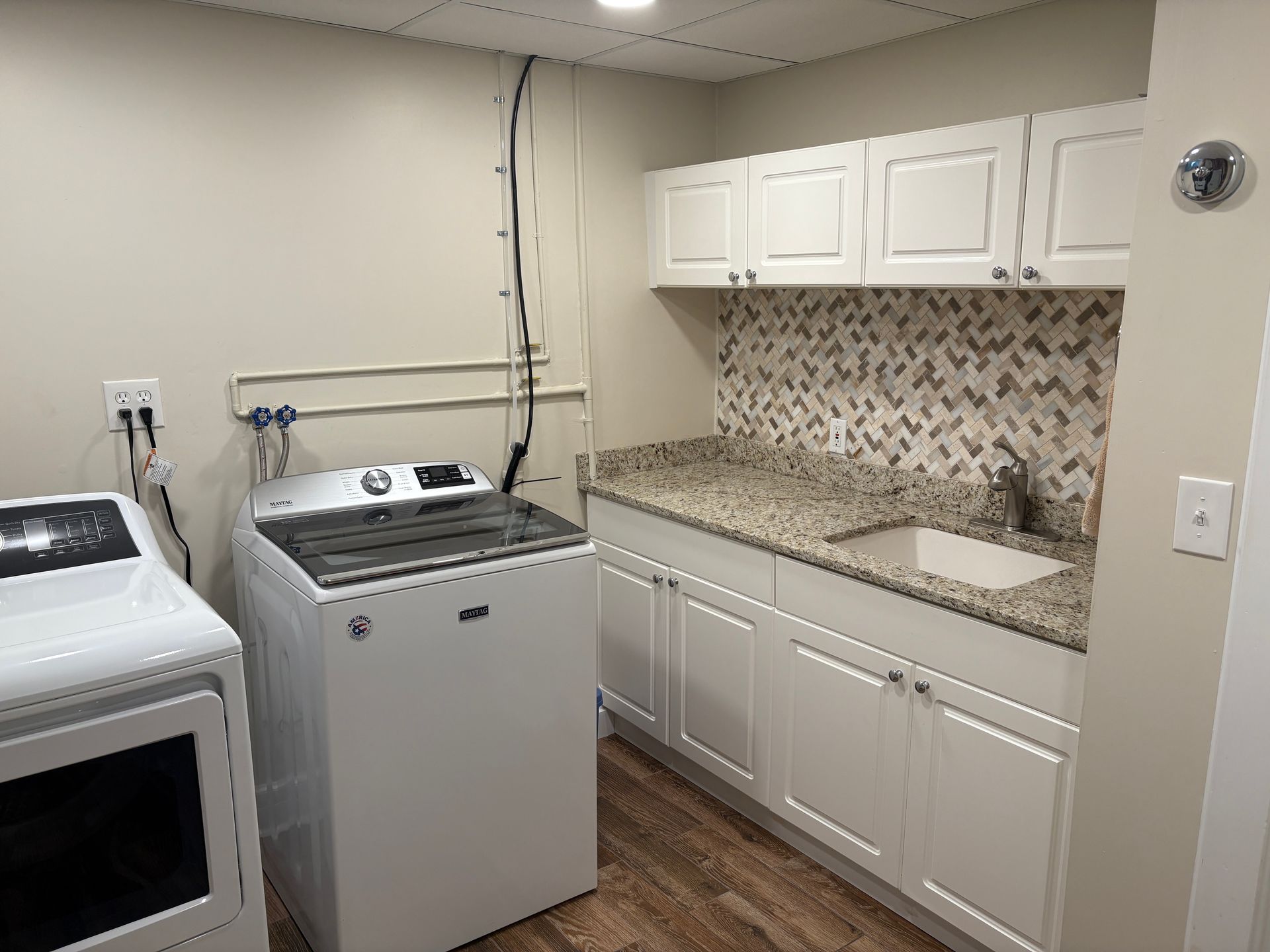 Laundry room with white appliances, cabinets, granite countertop, and patterned backsplash.
