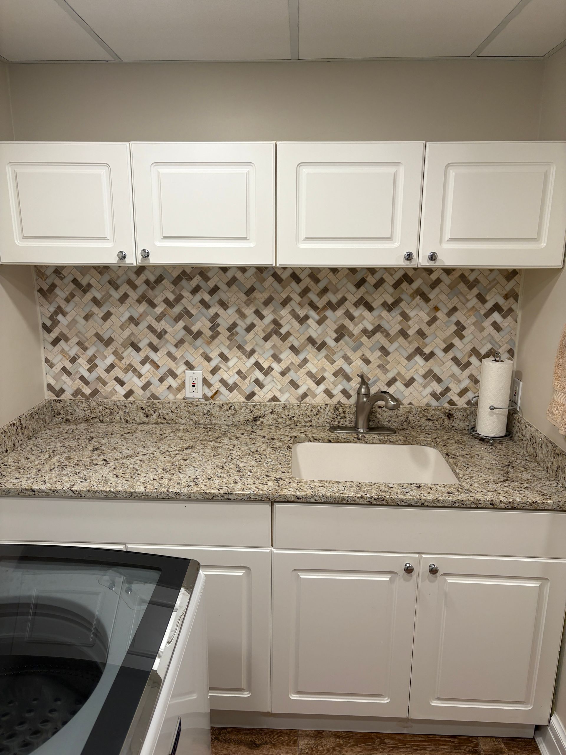 Laundry room with white cabinets, speckled countertop, tiled backsplash, and sink.