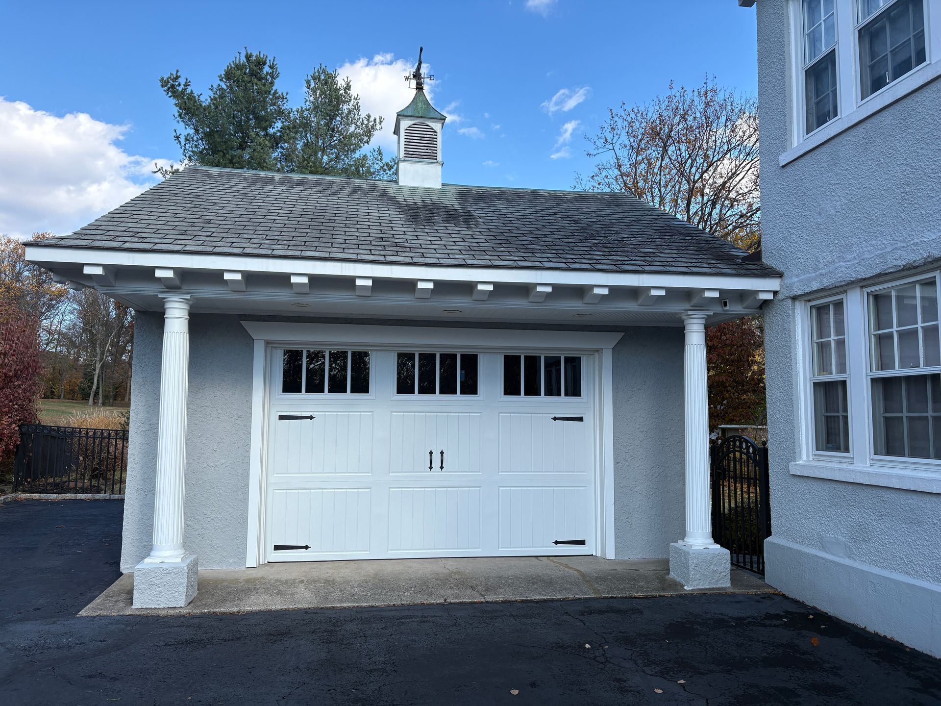 White garage with textured gray exterior, ornate columns, and a cupola; next to a stucco house.