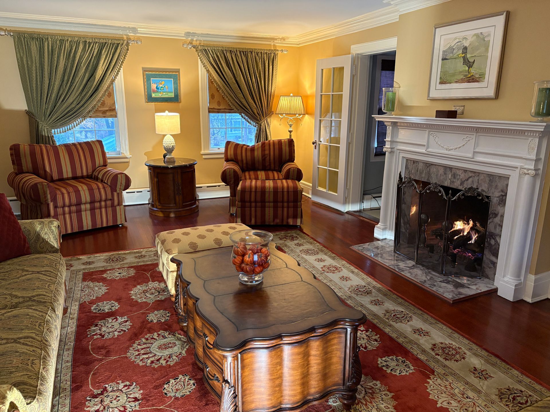 Cozy living room with fireplace, red patterned rug, two armchairs, and a decorative coffee table.