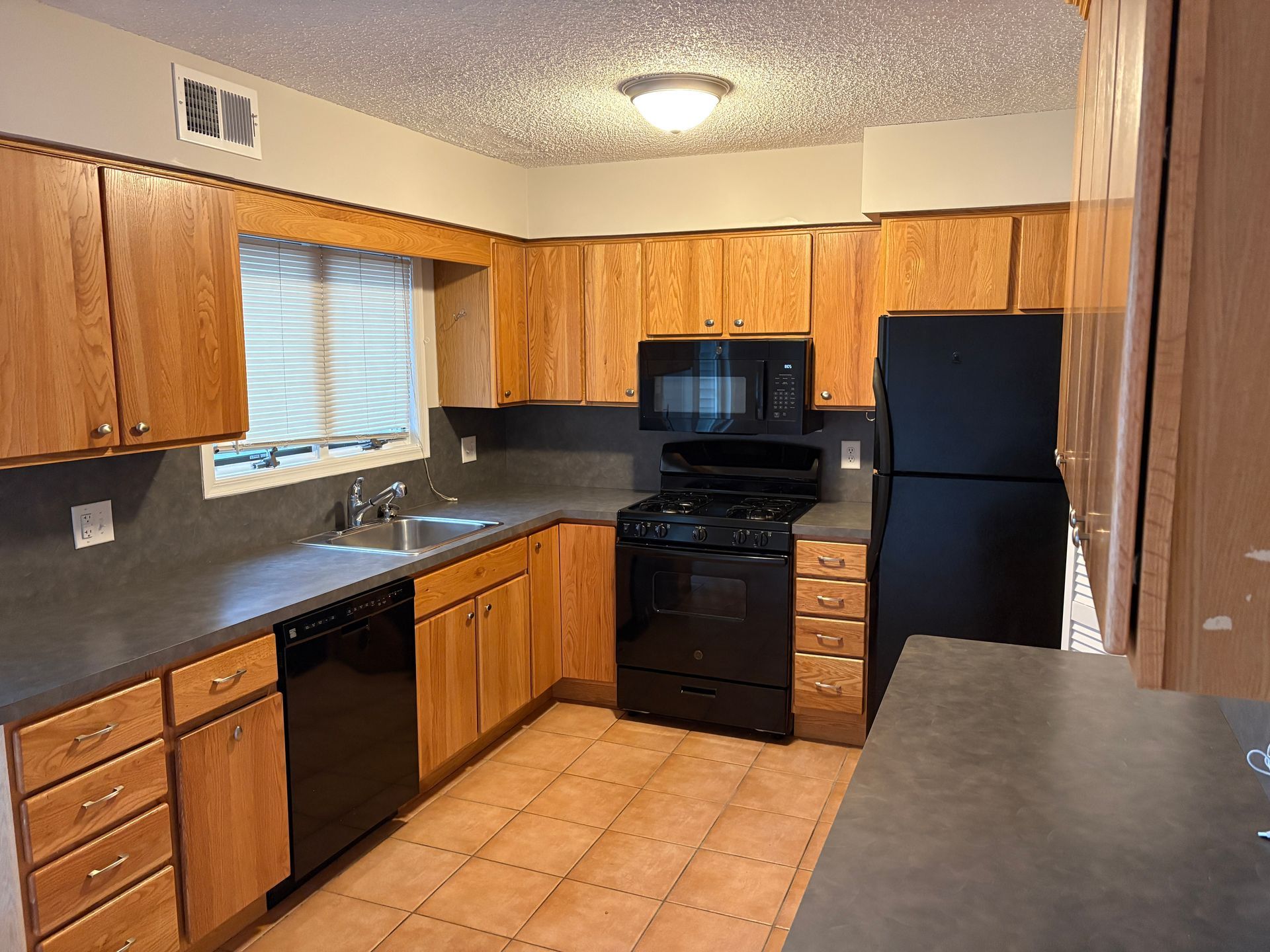 Kitchen with wood cabinets, black appliances, and gray countertops.