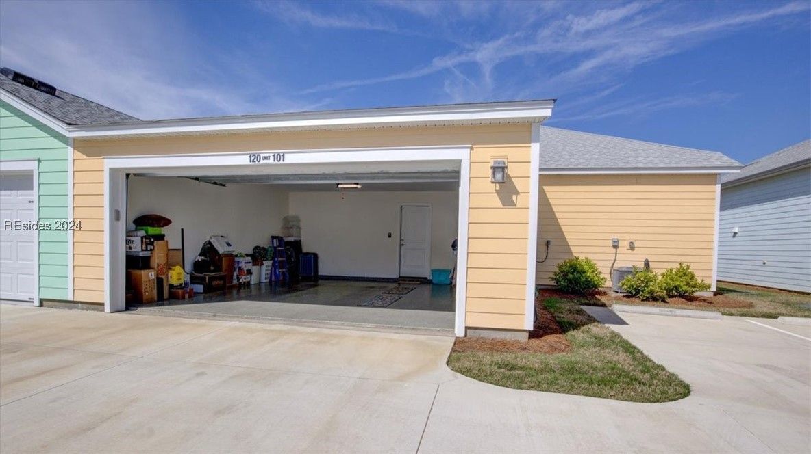 Open garage with various items inside, attached to a yellow house, blue sky above.