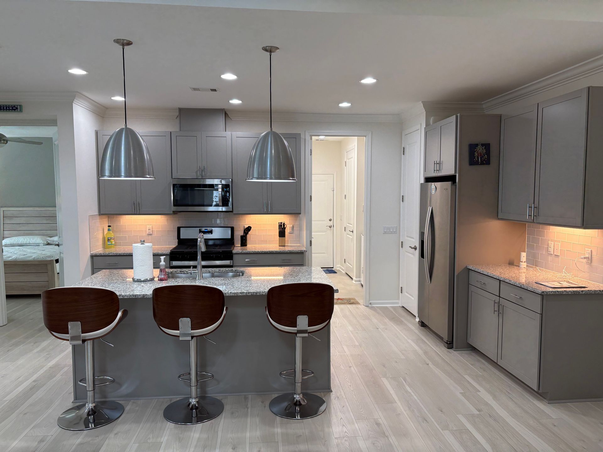 Modern kitchen with gray cabinets, island with stools, stainless steel appliances, and wood floor.