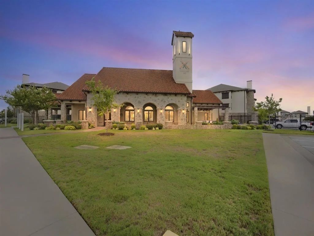 A Mediterranean-style building with a tower, a tiled roof, and a grassy lawn at sunset.