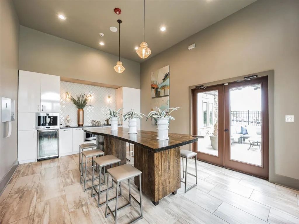 Modern kitchen area with a large island, stools, and white cabinetry. French doors lead to an outdoor patio.