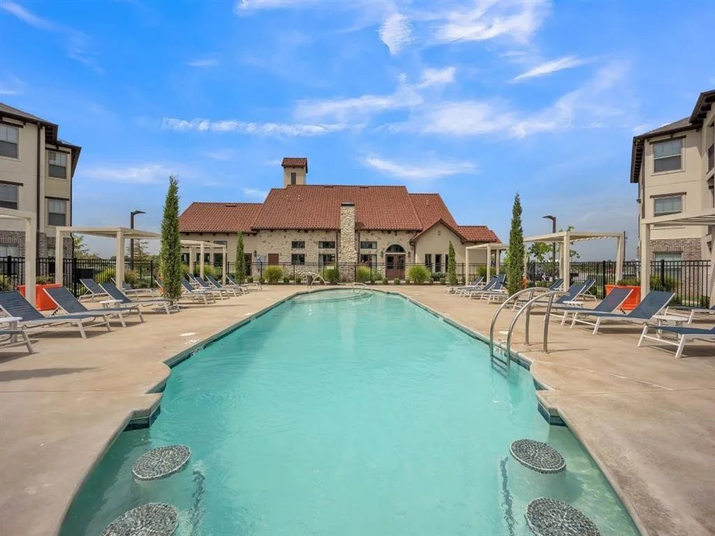 Pool surrounded by lounge chairs, in front of a clubhouse with red-tiled roof, under a blue sky.
