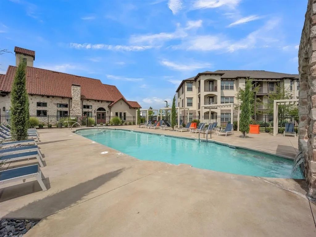 Swimming pool and lounge chairs in front of apartment buildings under a blue sky.