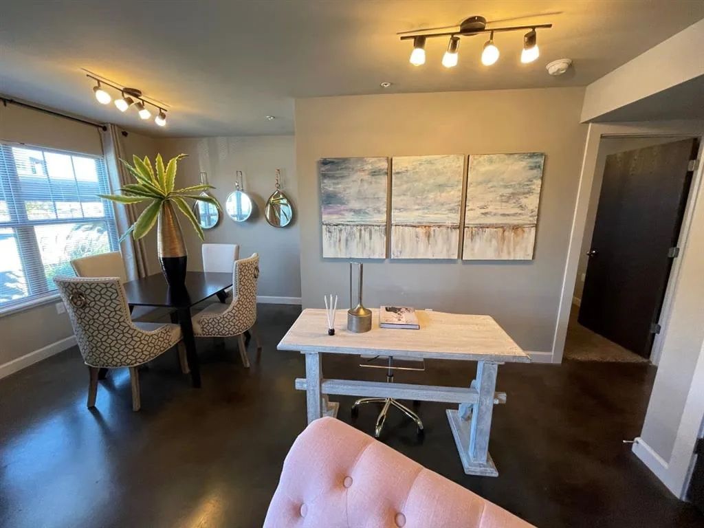 A dining area with a table, patterned chairs, and abstract art on the wall. A doorway leads to another room.