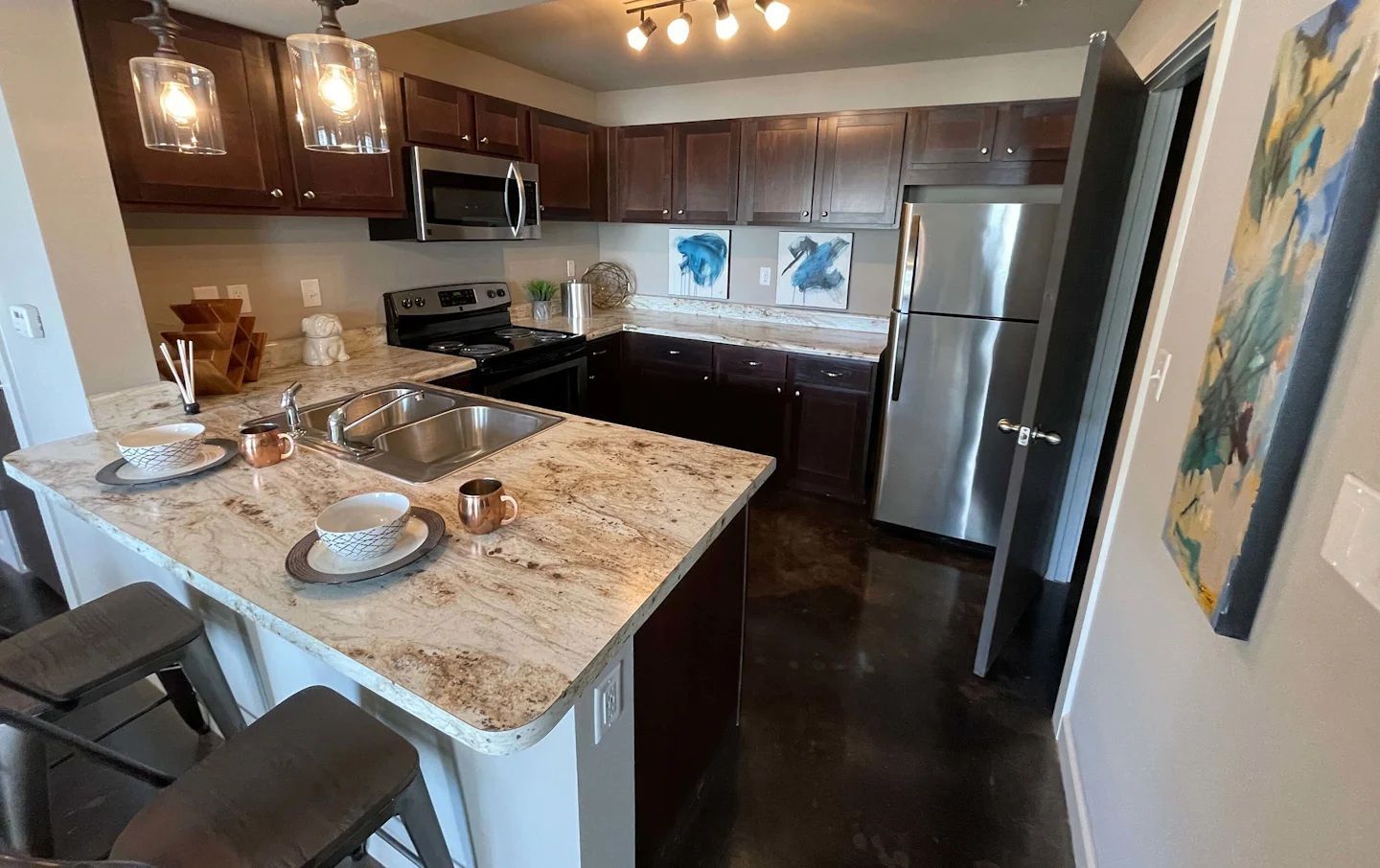 Kitchen with dark brown cabinets, stainless steel appliances, granite countertops, and two stools.