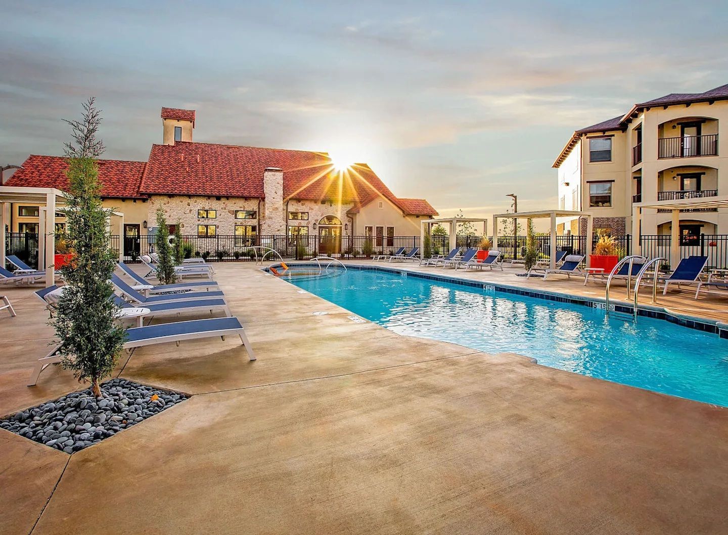 Poolside view of a building with a red-tiled roof and lounge chairs.