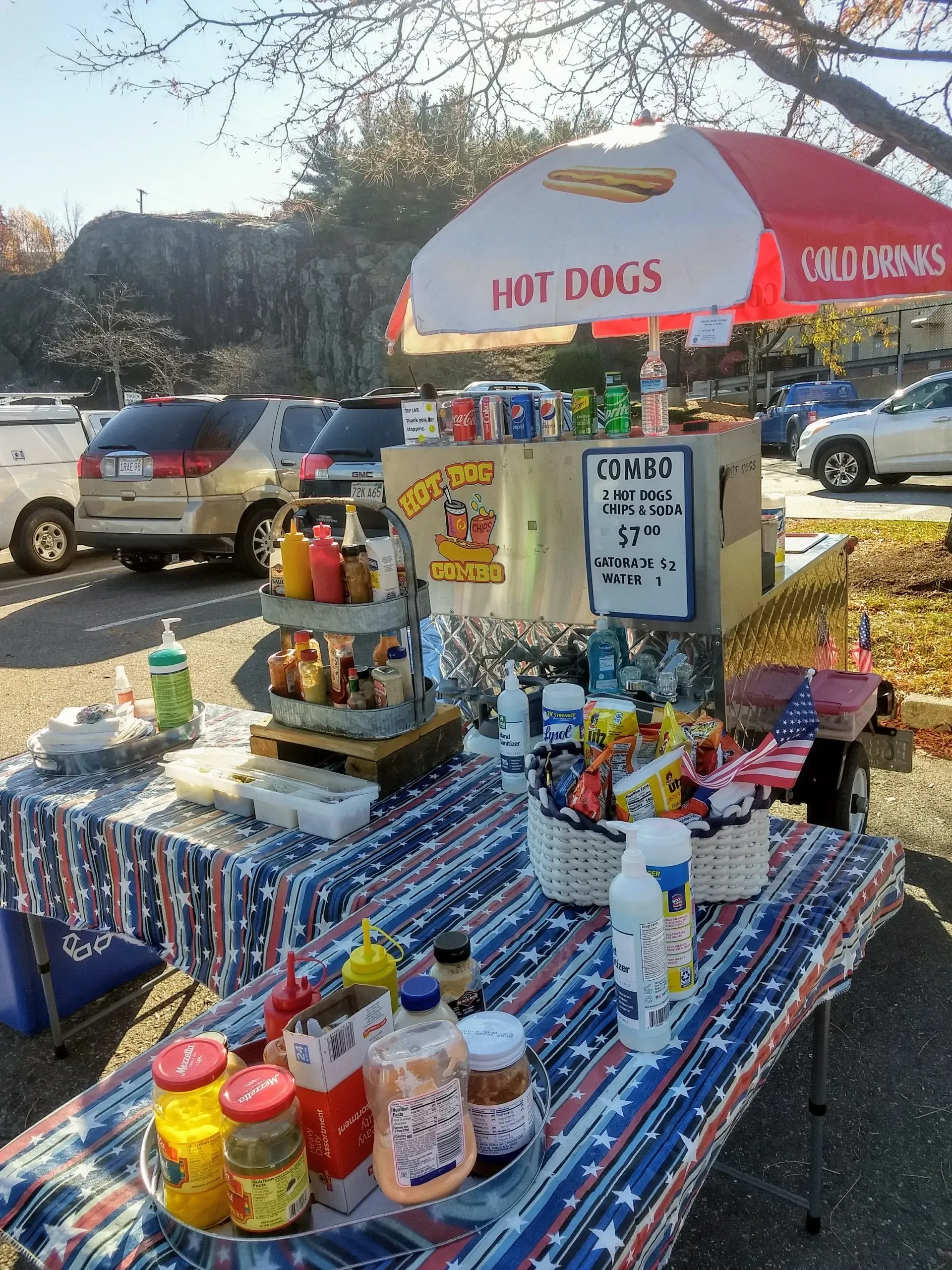 A table with condiments and an umbrella that says hot dogs