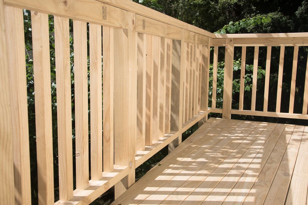 A Wooden Deck With a Railing and Trees in the Background — Green Thumb Landscapes In Coffs Harbour, NSW