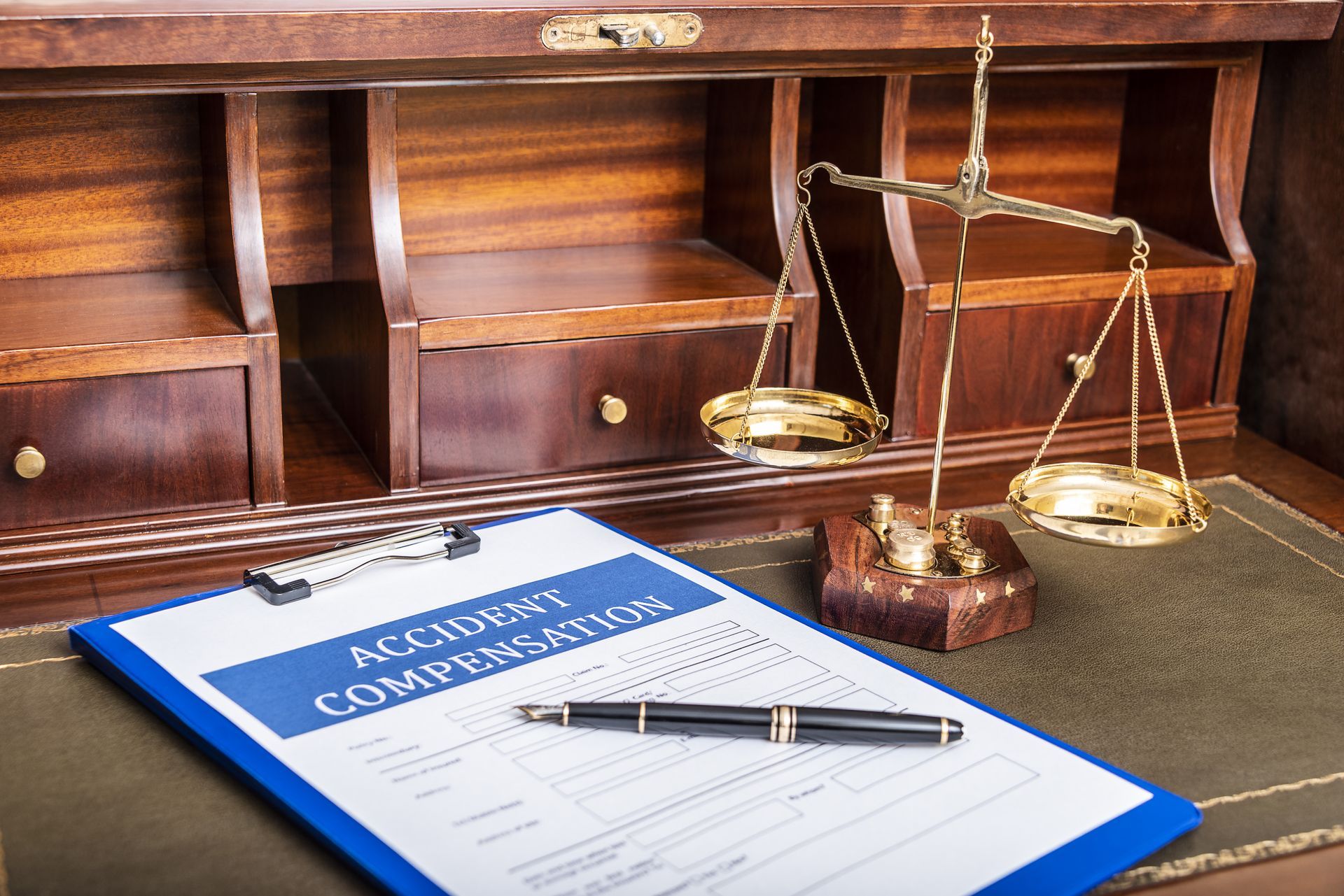 Accident compensation form on top of a wooden court desk with a pen and scales of justice next to it.