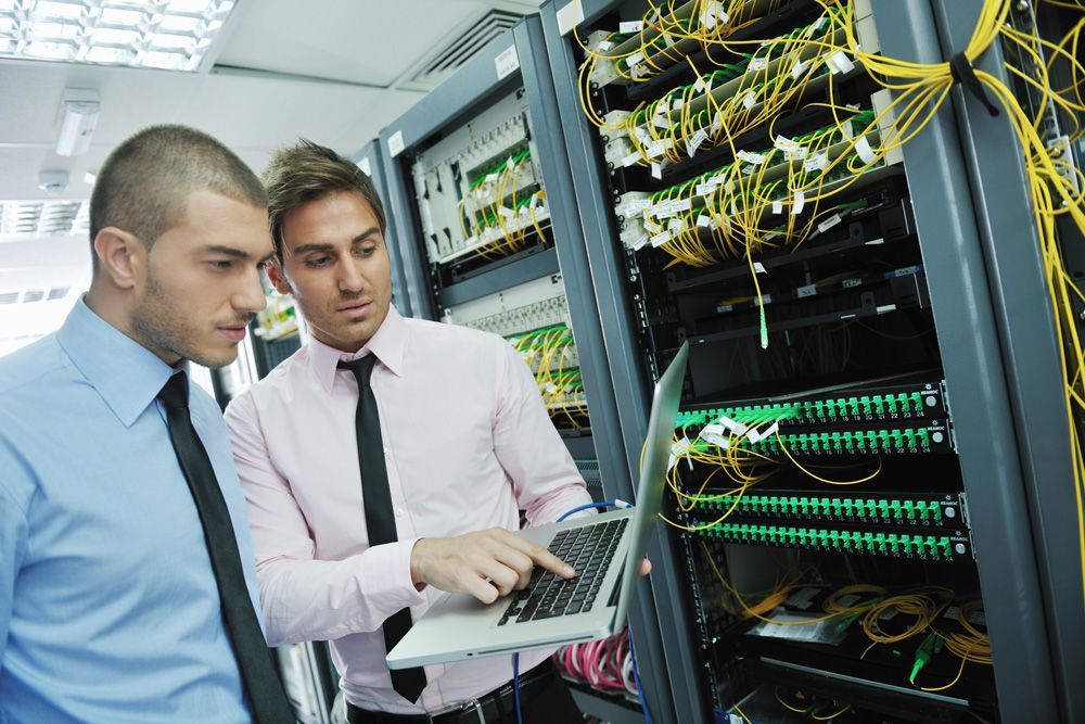 Two men are looking at a laptop in a server room.