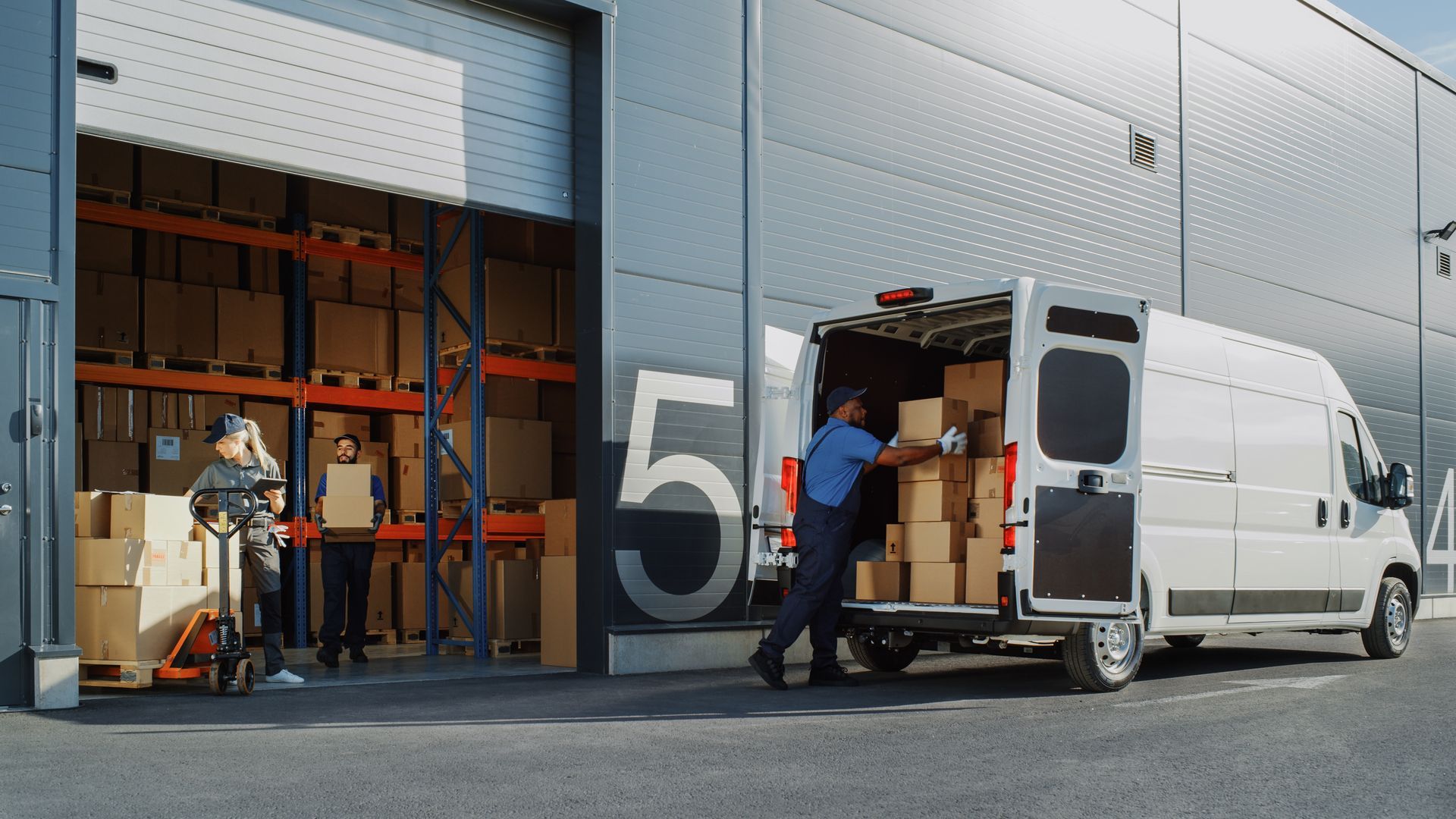 A man is loading boxes into a van in front of a warehouse.