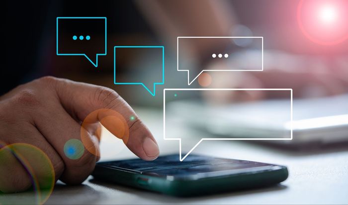 A person is using a smart phone with speech bubbles coming out of it.