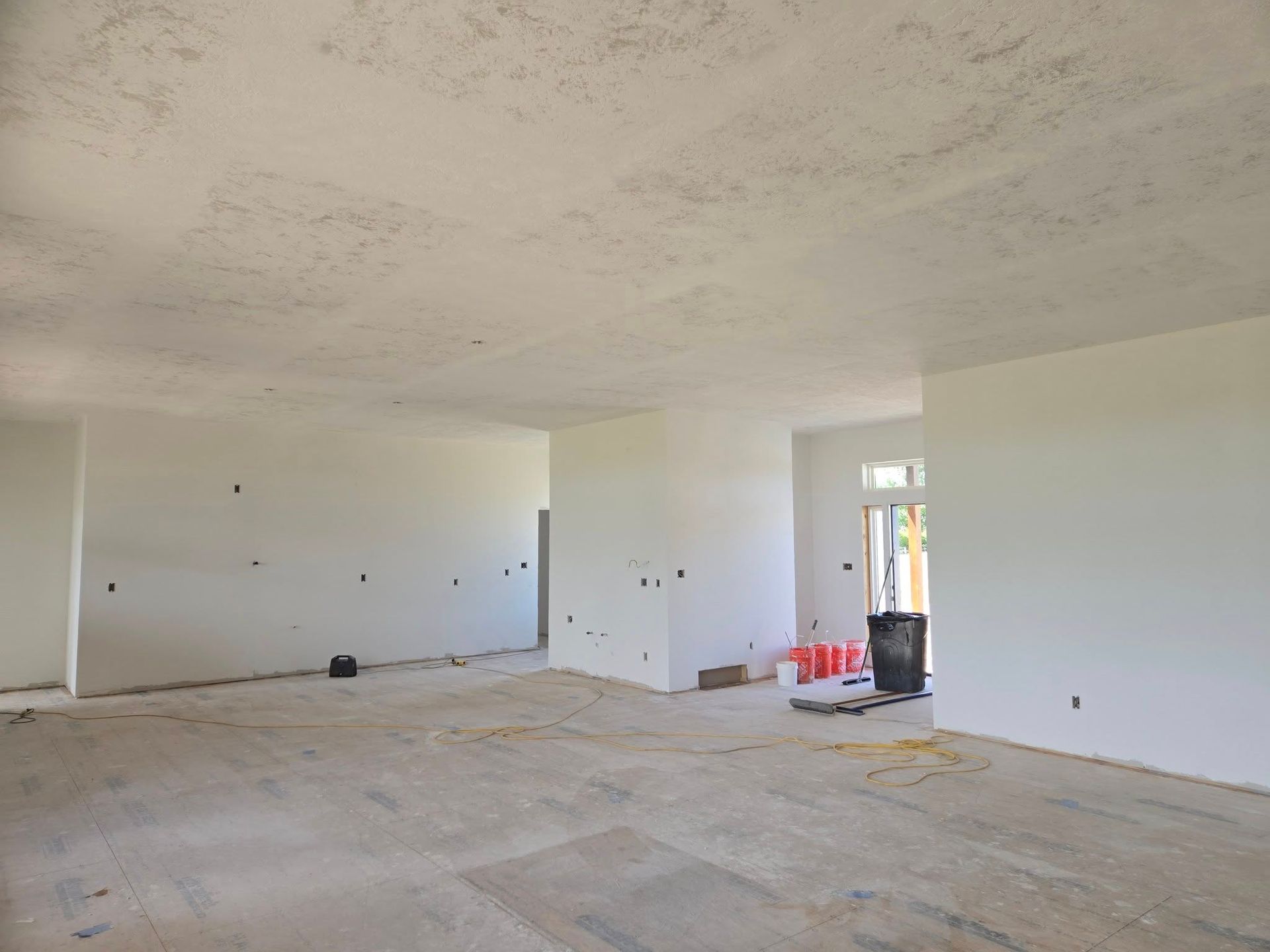 Empty room under construction with white walls and textured ceiling; bare concrete floor.