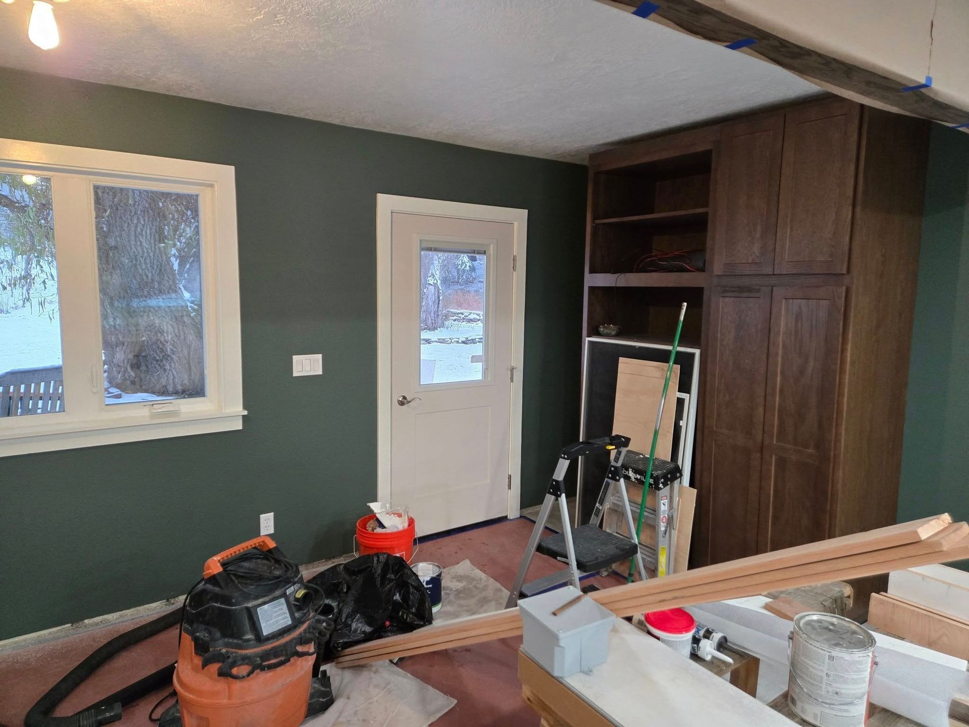 Interior room with dark green walls, white door/window trim, and brown cabinets. Construction materials are present.