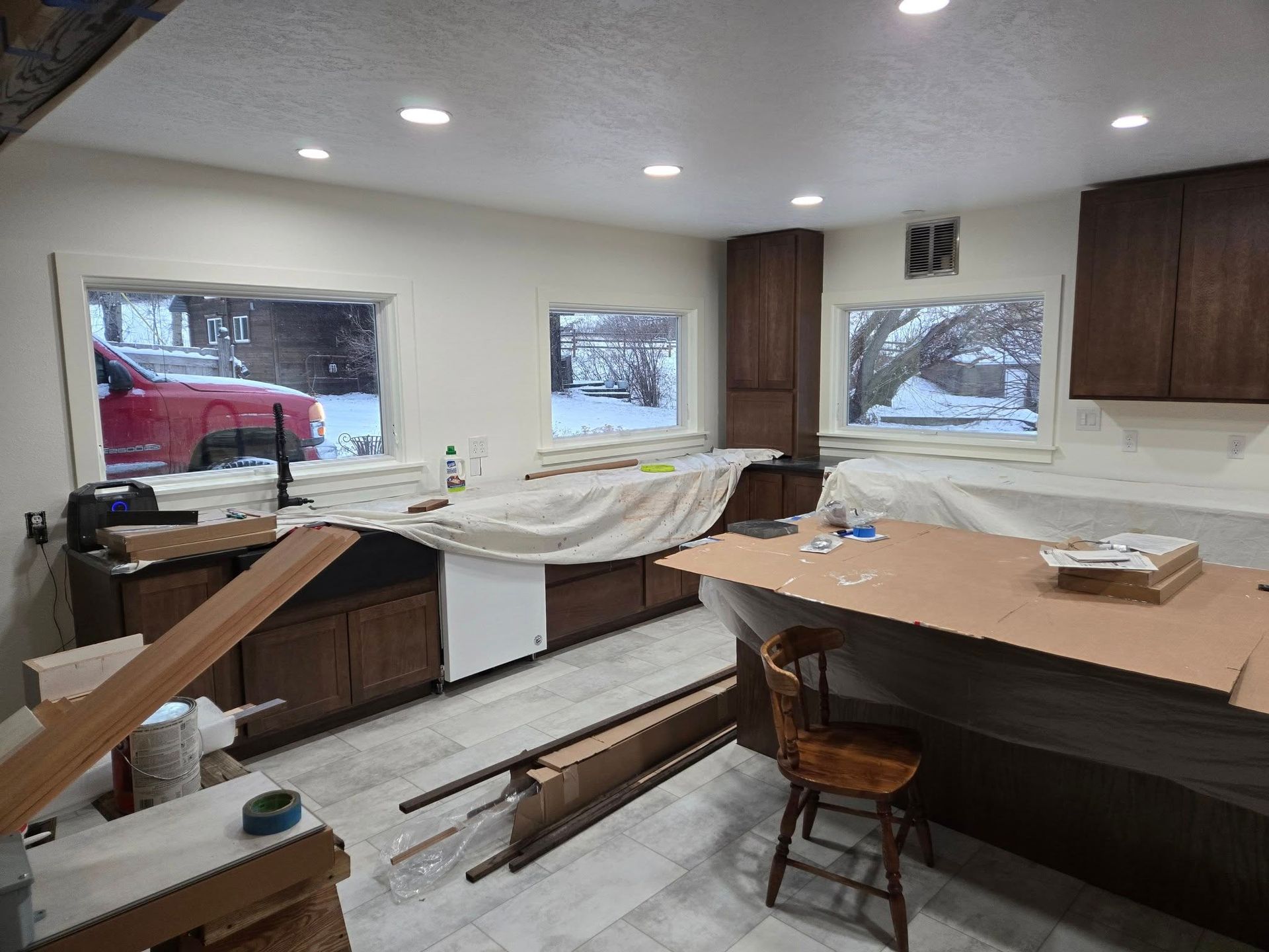 Kitchen under renovation with dark brown cabinets, light countertops, and snowy windows.