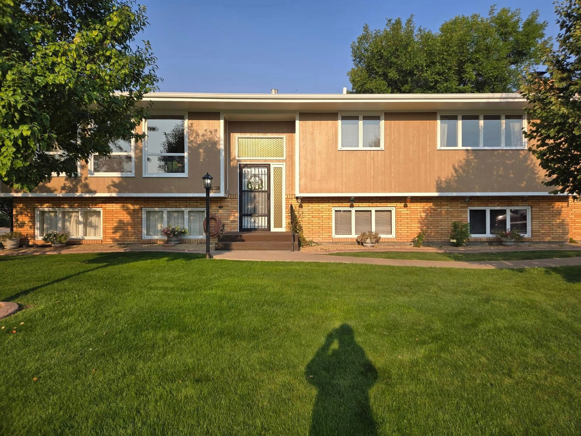 Two-story house with tan siding, white windows, and green lawn.