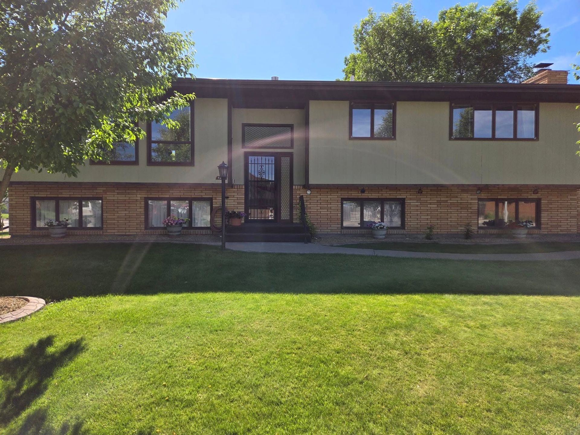 Two-story house with green siding and brick, set on a grassy lawn under a sunny sky.