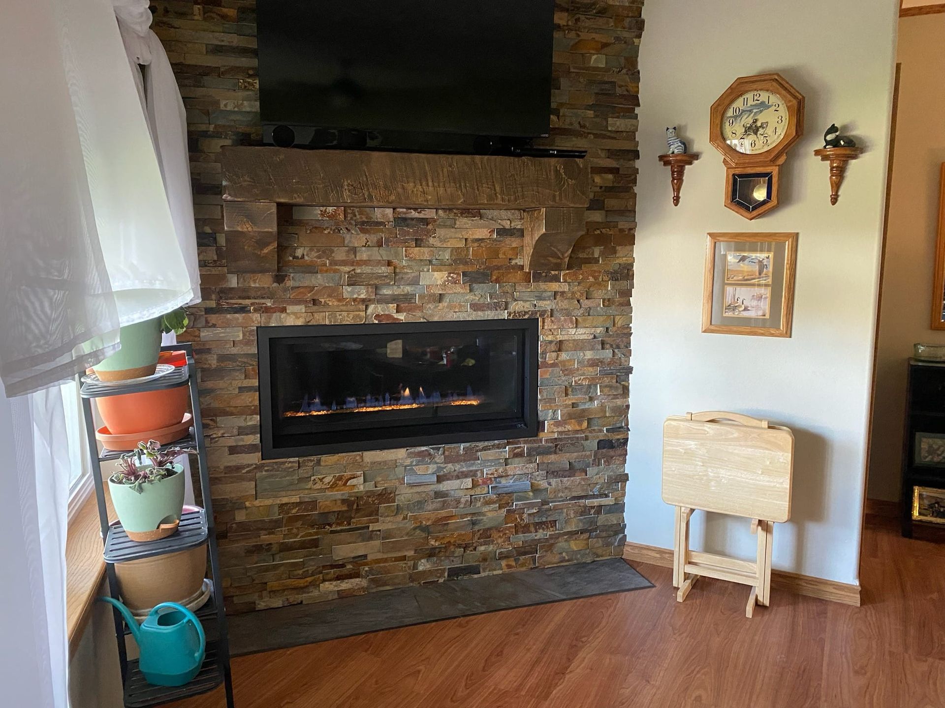 Fireplace with a stone facade, TV above, clock, and folding table on wooden floor.