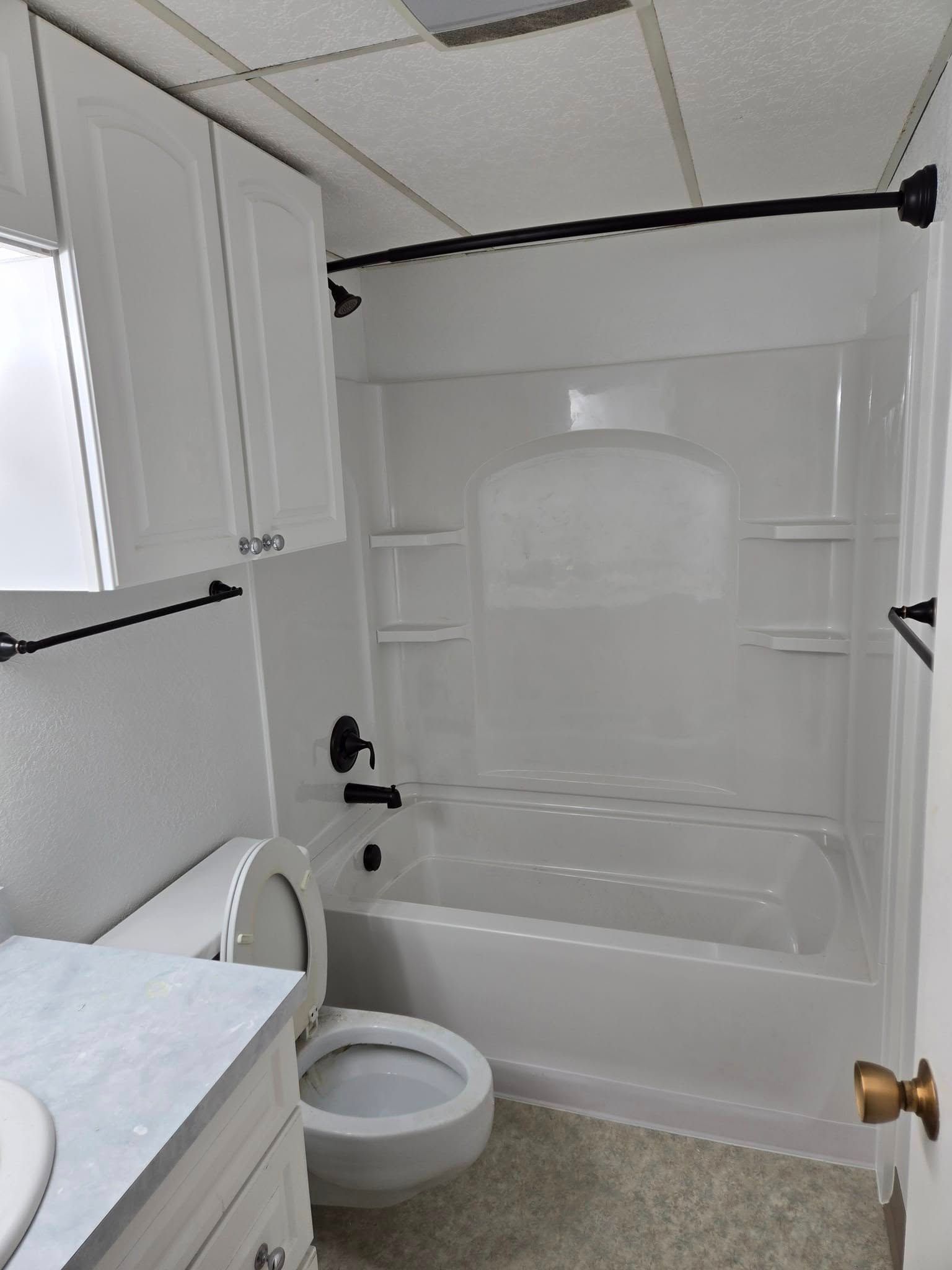 White bathroom with tub, toilet, sink, cabinets, and black fixtures.