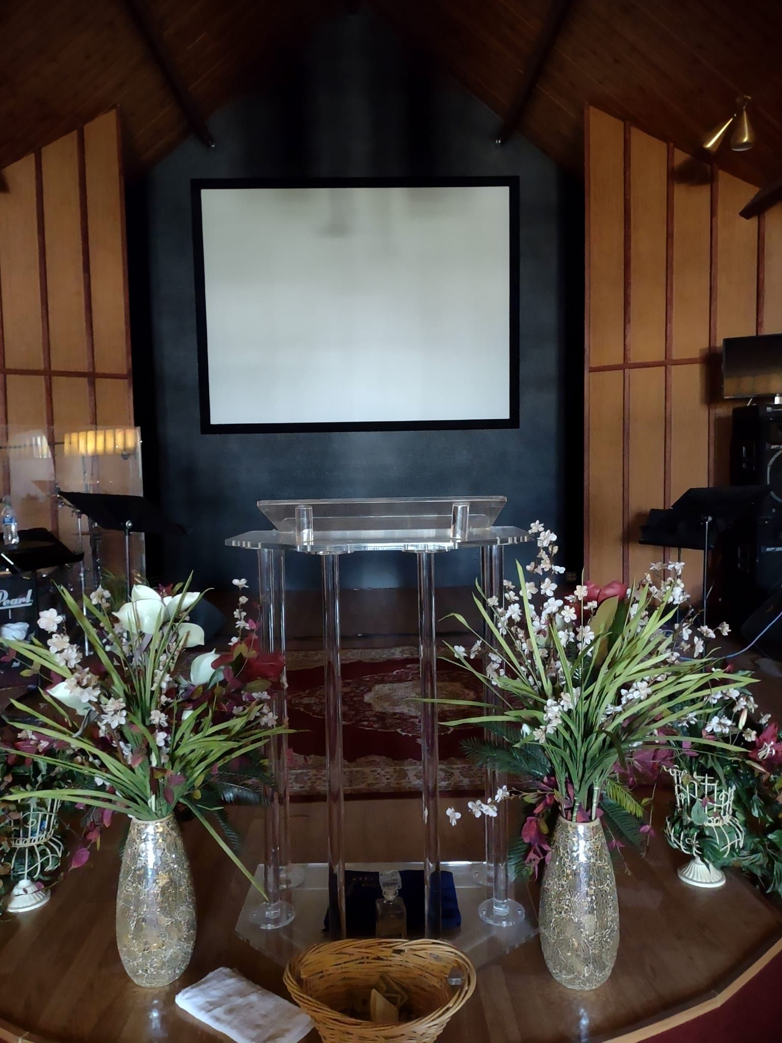 Church altar with a clear podium, floral arrangements, and a projection screen.