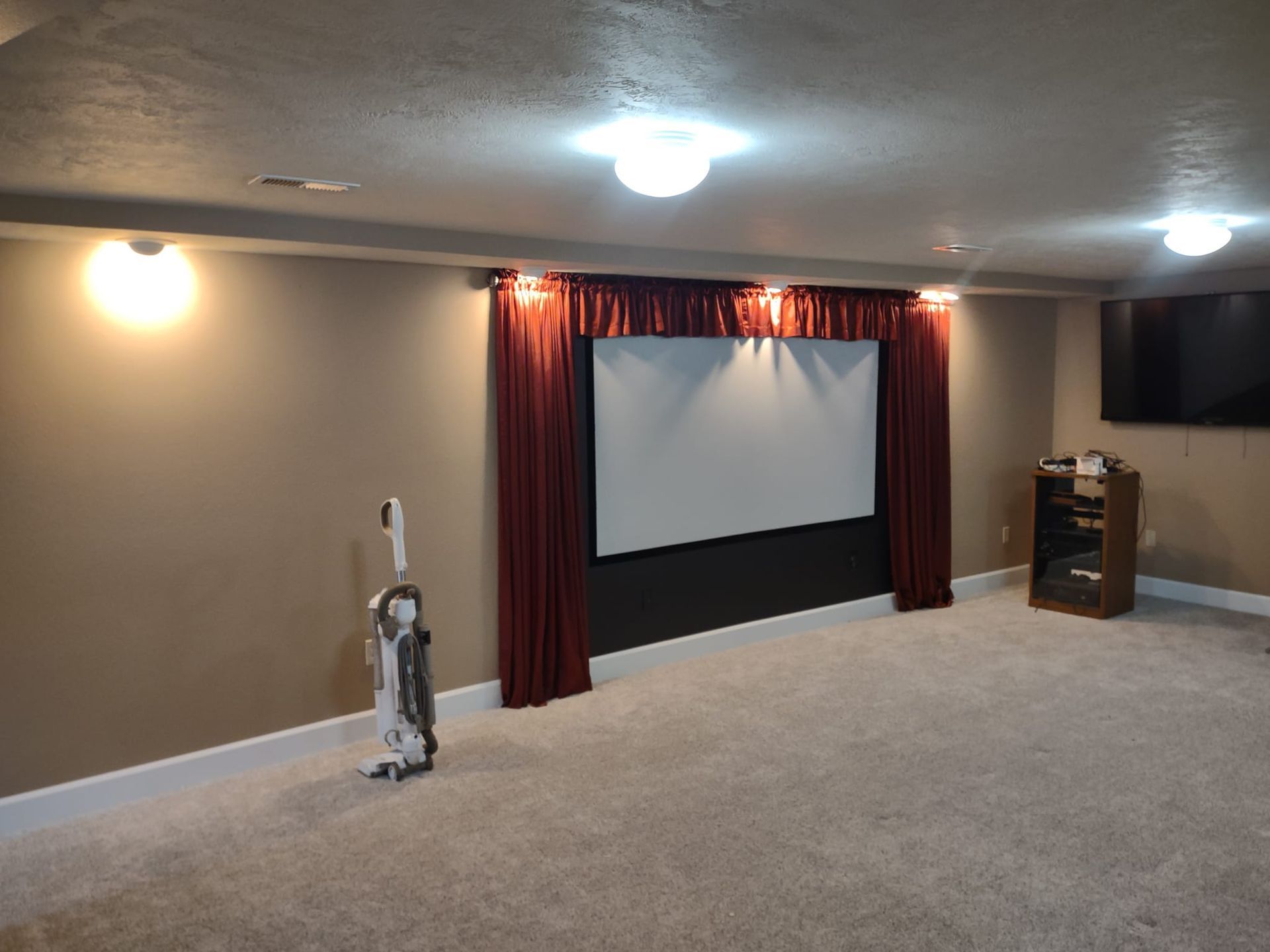 Home theater with projection screen, red curtains, and a vacuum cleaner.