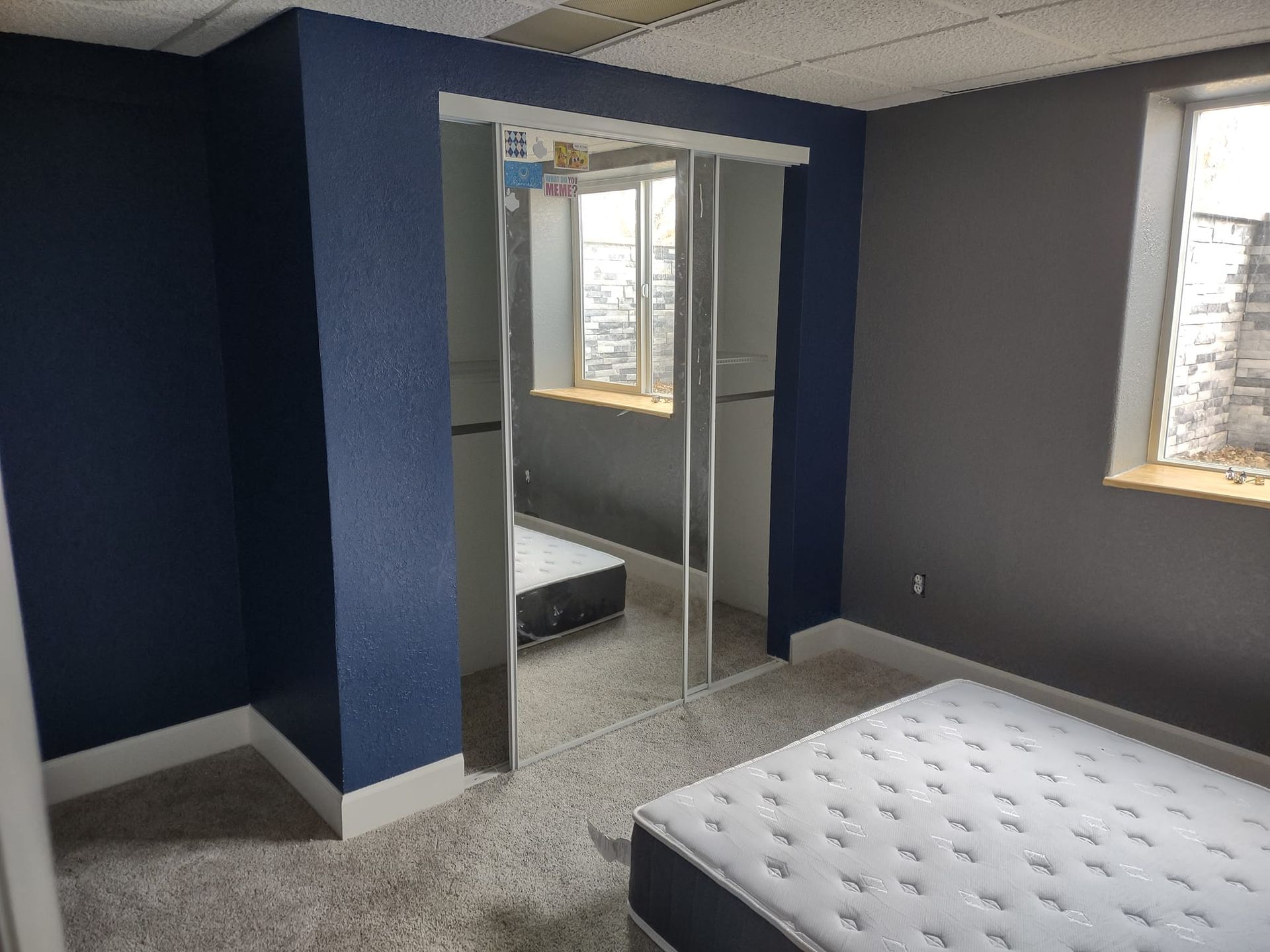 A bedroom with blue and gray walls, a mirrored closet, and a mattress on the floor.