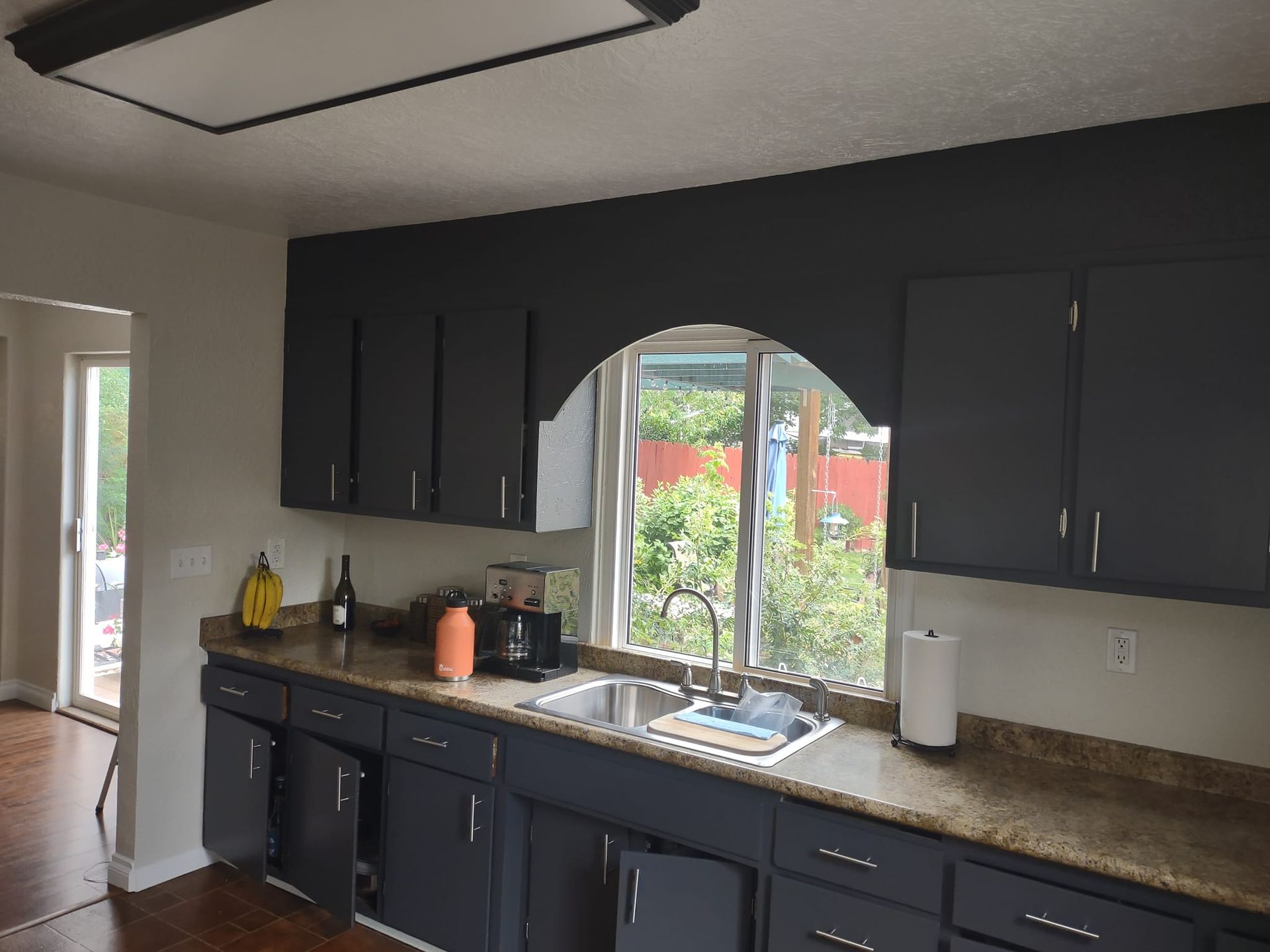 Dark gray kitchen cabinets with an arched window overlooking a yard.