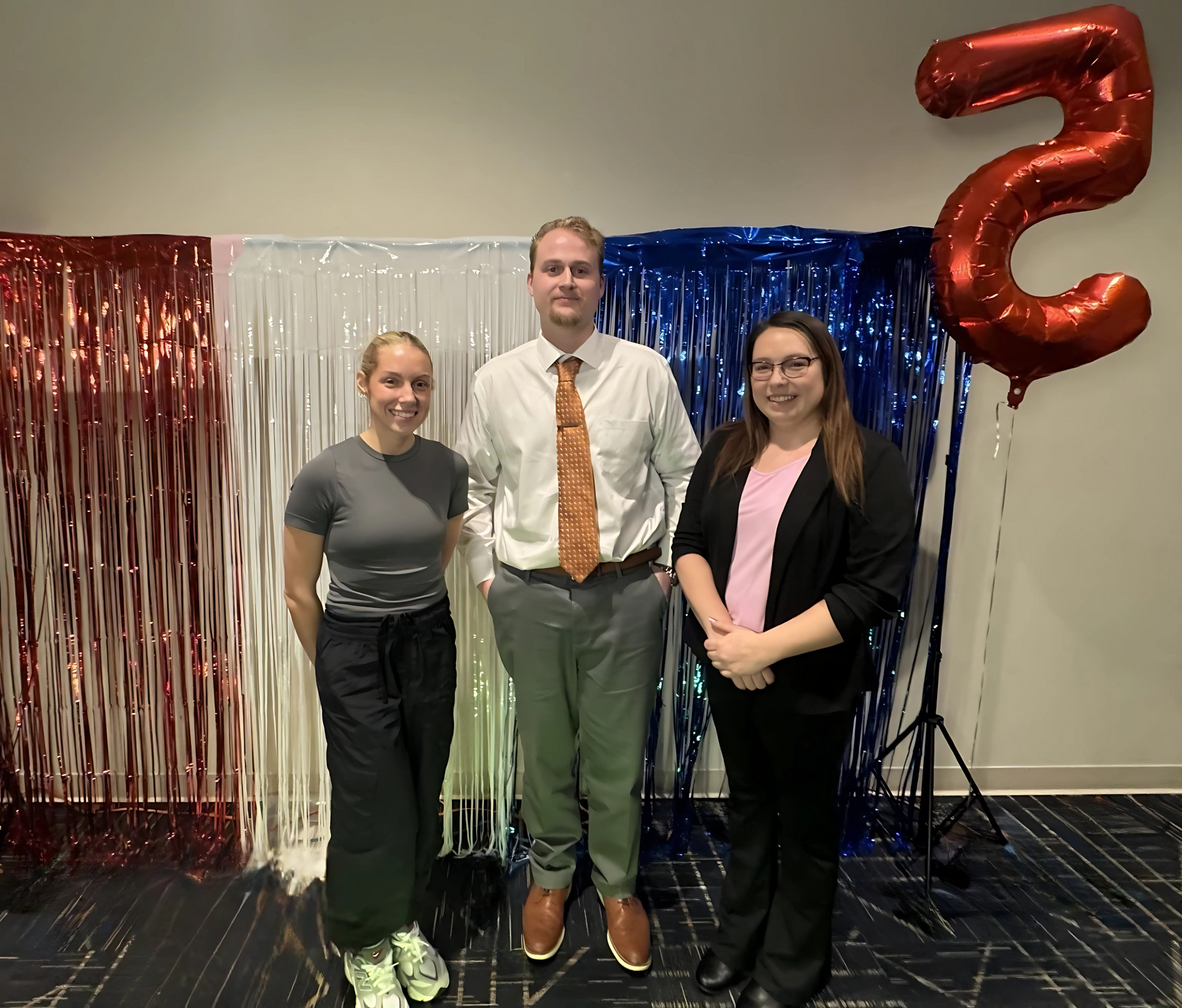 A man and two women are posing for a picture in front of a red number 5 balloon.