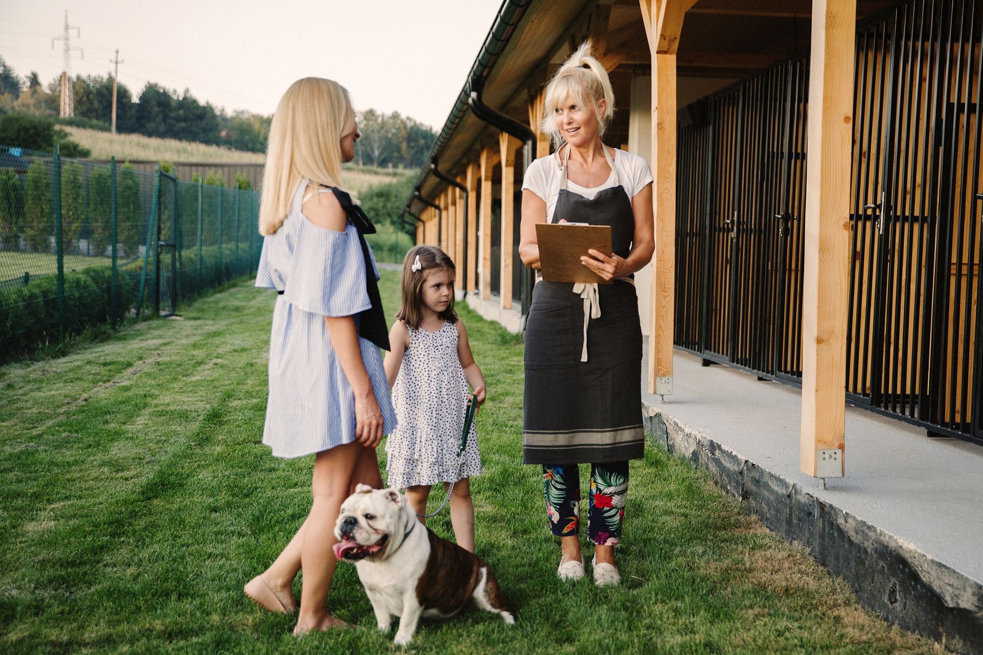 A woman is holding a clipboard and talking to two girls and a dog.