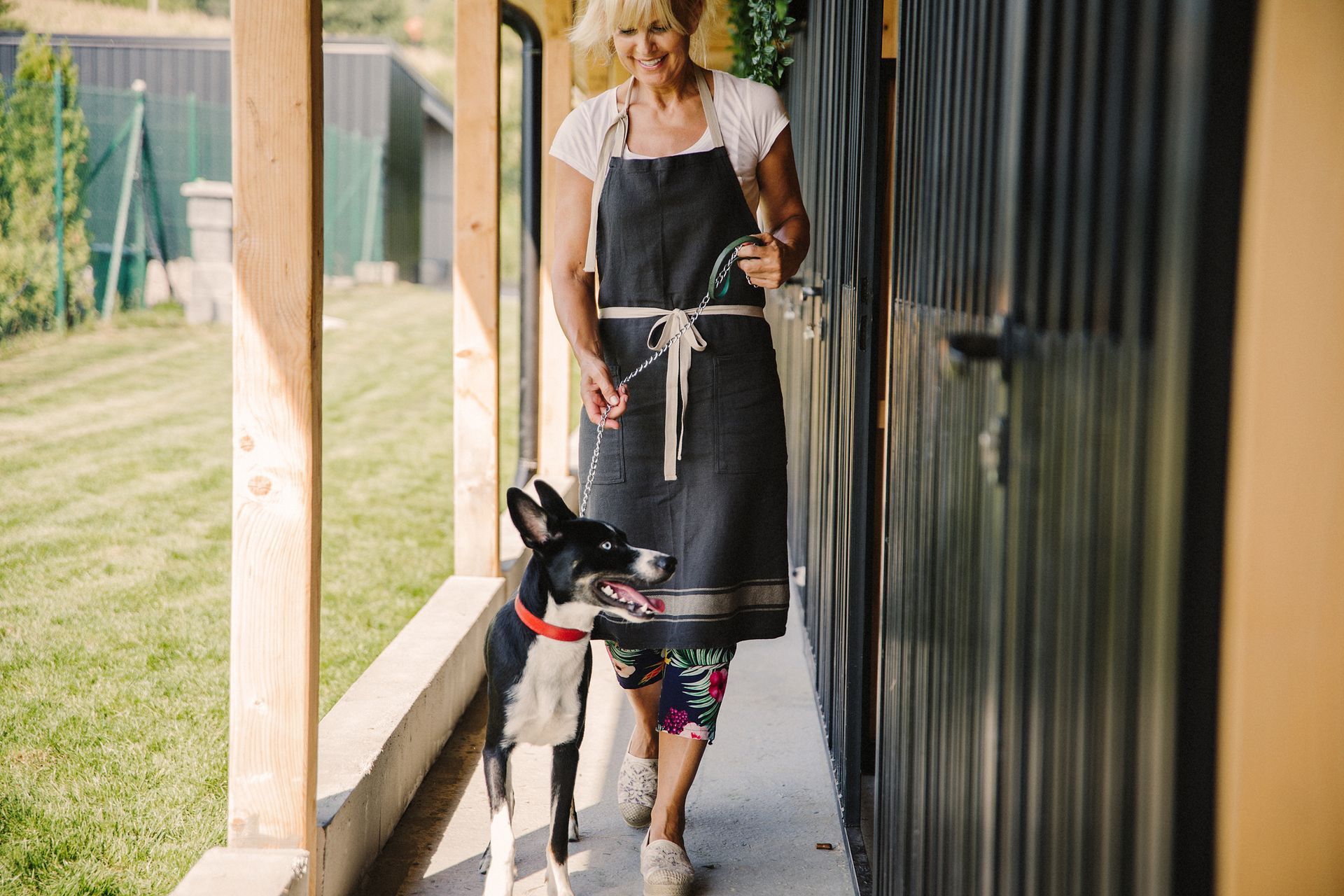 A woman is walking a dog on a leash on a porch.