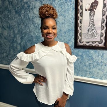 A woman in a white off the shoulder top is standing in front of a blue wall.