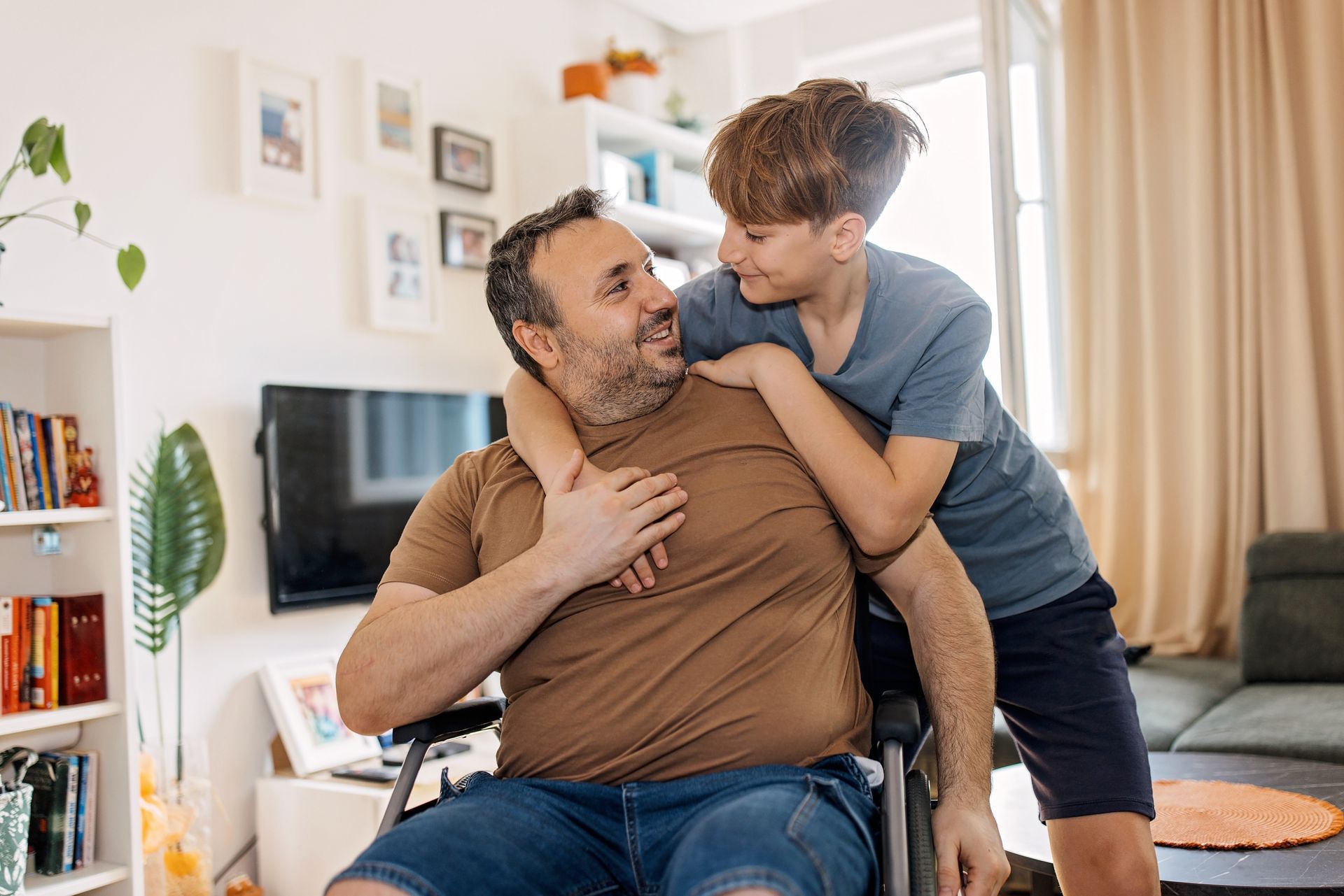 A boy is standing next to a man in a wheelchair.