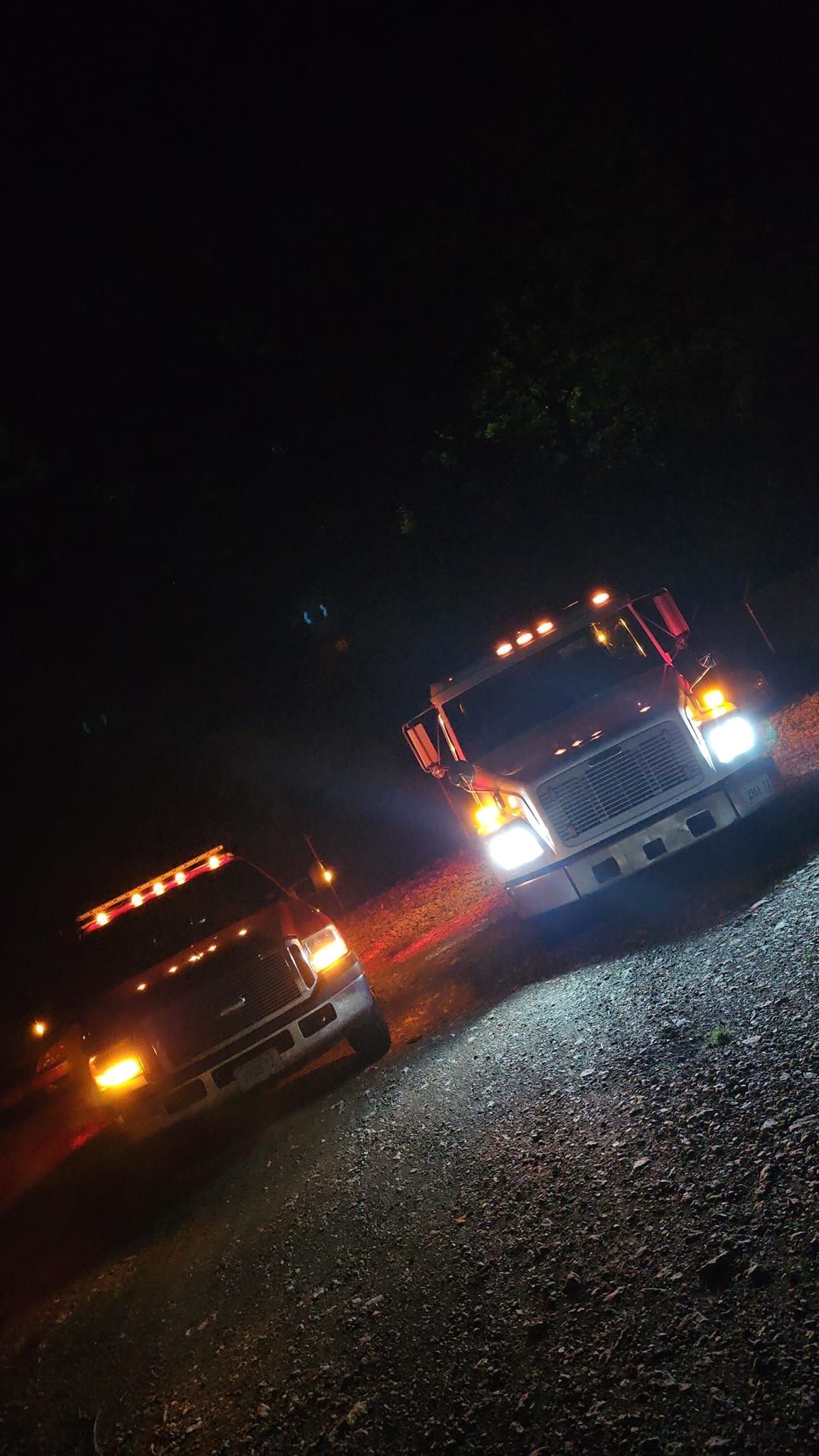 Two trucks are parked next to each other on a gravel road at night.