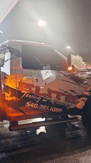 A tow truck is covered in snow at night.